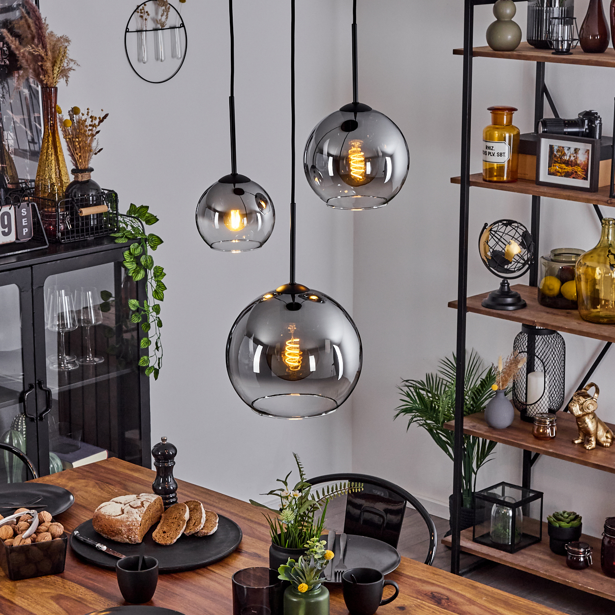 Esszimmer mit Holztisch und drei hängenden Kugelleuchten mit sichtbaren Glühbirnen.
