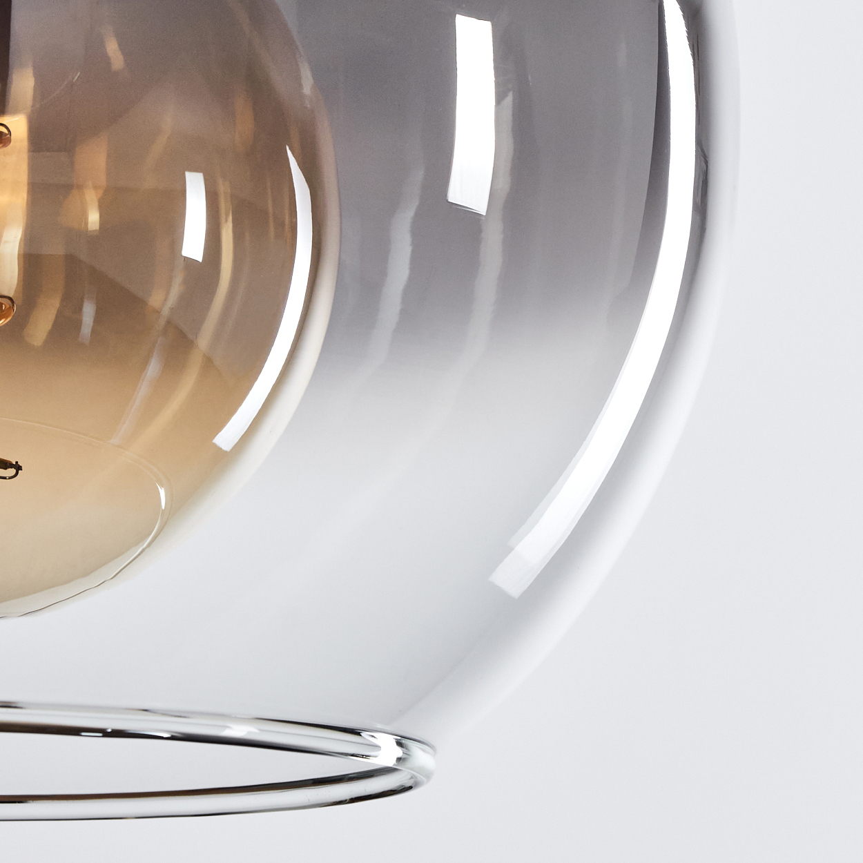 Nahaufnahme eines Lampenschirms aus Glas mit silbernem Metallrand. Die Glühbirne leuchtet.