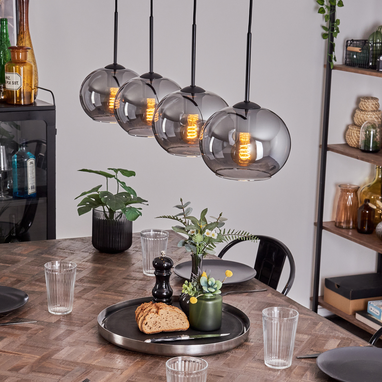 Esszimmer mit fünf Pendelleuchten mit rauchgrauen Glaskugelschirmen. Tischdeko und Pflanzen sind sichtbar.