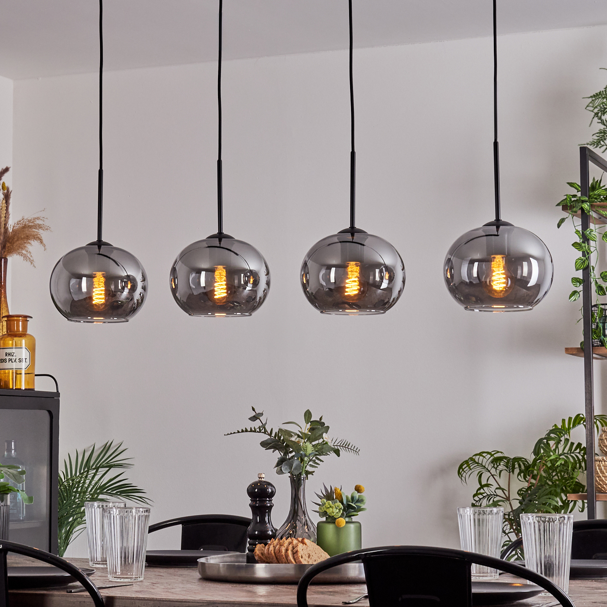Esszimmer mit vier Pendelleuchten mit rauchgrauen Glaskugelschirmen. Tischdeko und Pflanzen sind sichtbar.