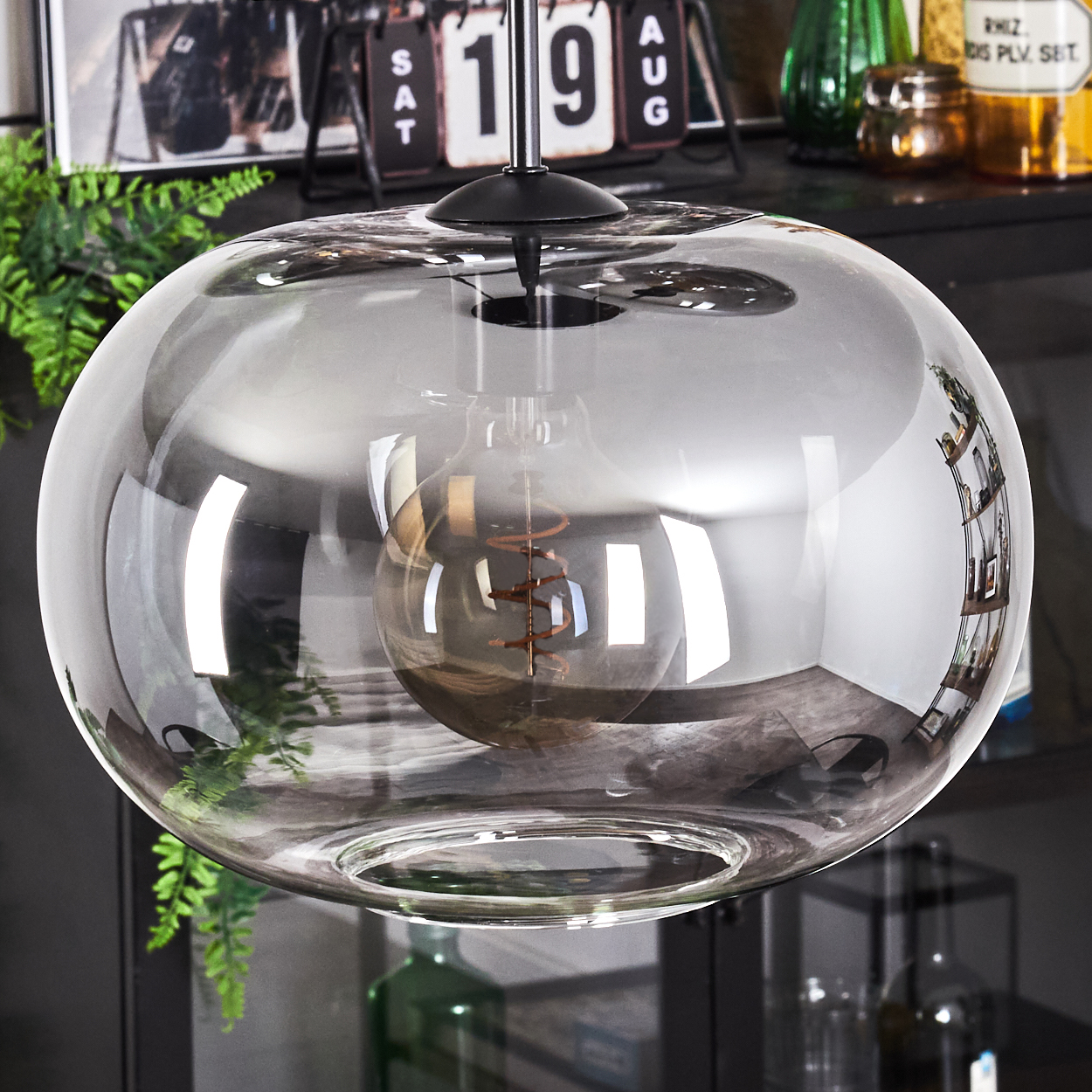 Nahaufnahme einer runden Glas-Hängeleuchte mit sichtbarer Glühbirne vor dunklem Hintergrund.
