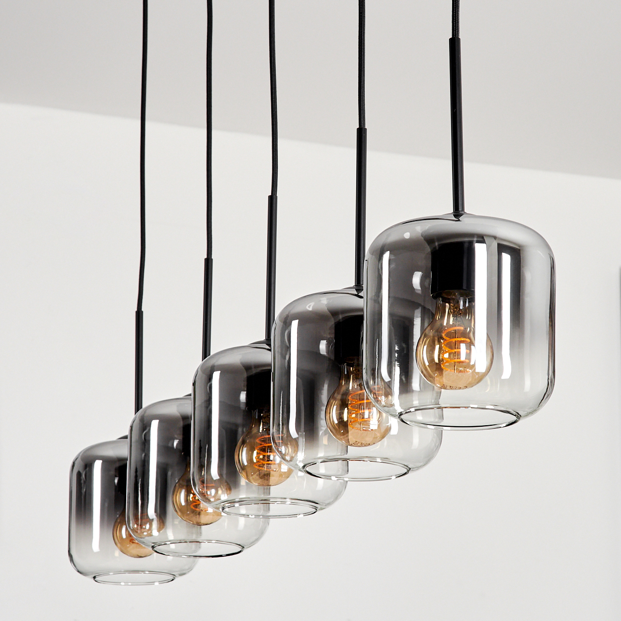Eine Reihe von fünf Pendelleuchten mit zylindrischen Glasschirmen, jede mit einer sichtbaren Glühbirne.