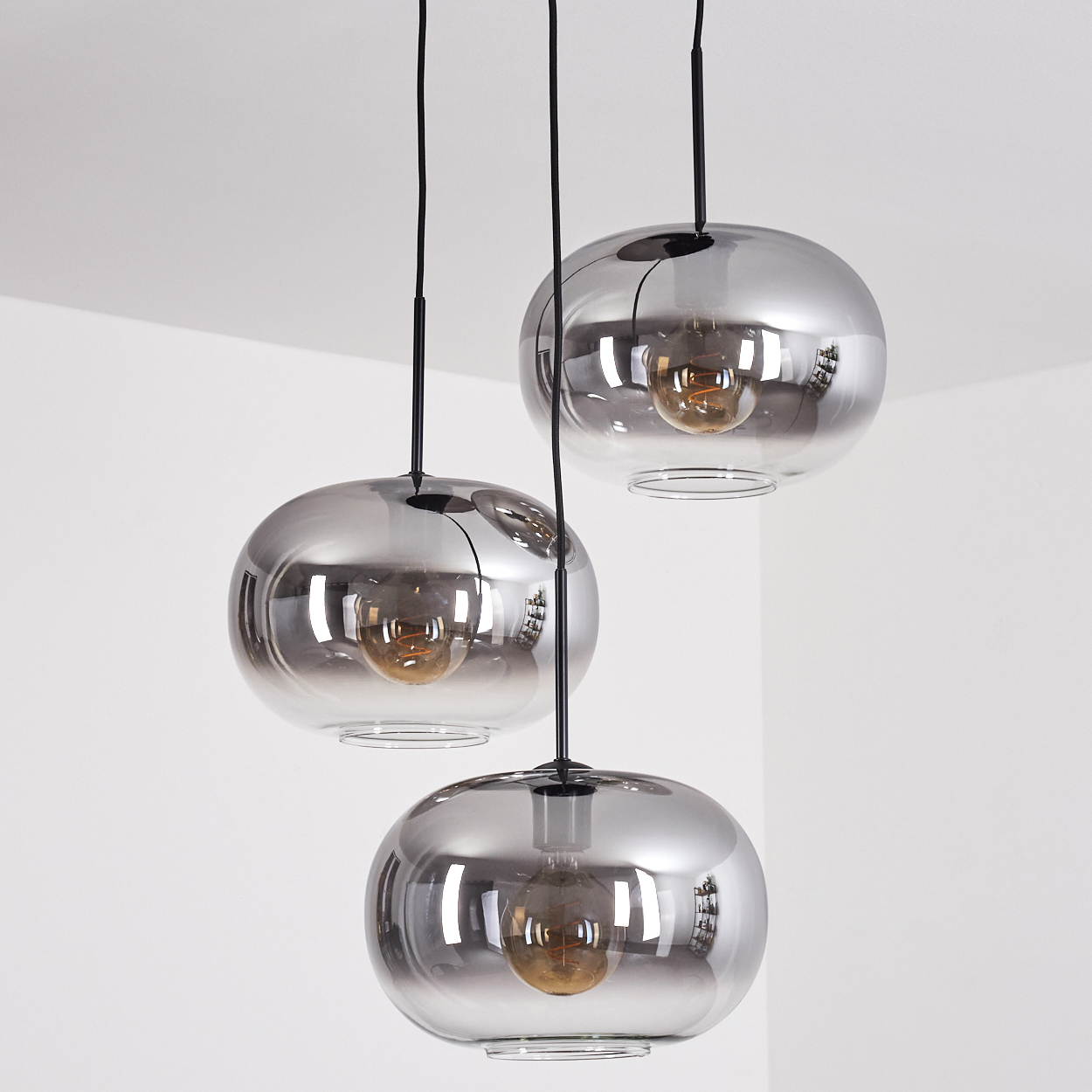 Drei Pendelleuchten mit runden Glasschirmen und sichtbaren Glühbirnen vor weißem Hintergrund.