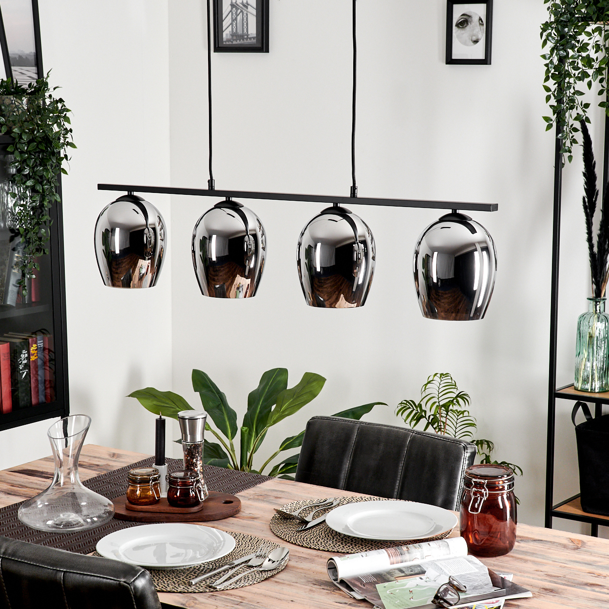 Esszimmer mit Holztisch, Hängelampen, Pflanzen und Dekorationen. Vier reflektierende Lichter hängen über dem Tisch.