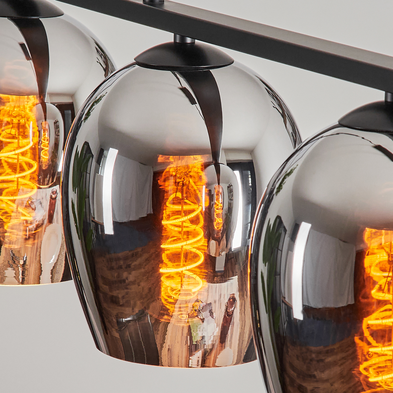 Nahaufnahme von drei kugelförmigen Lampen, jede mit einer sichtbaren, glühenden orangefarbenen Glühbirne. Die Lampen reflektieren den Raum.