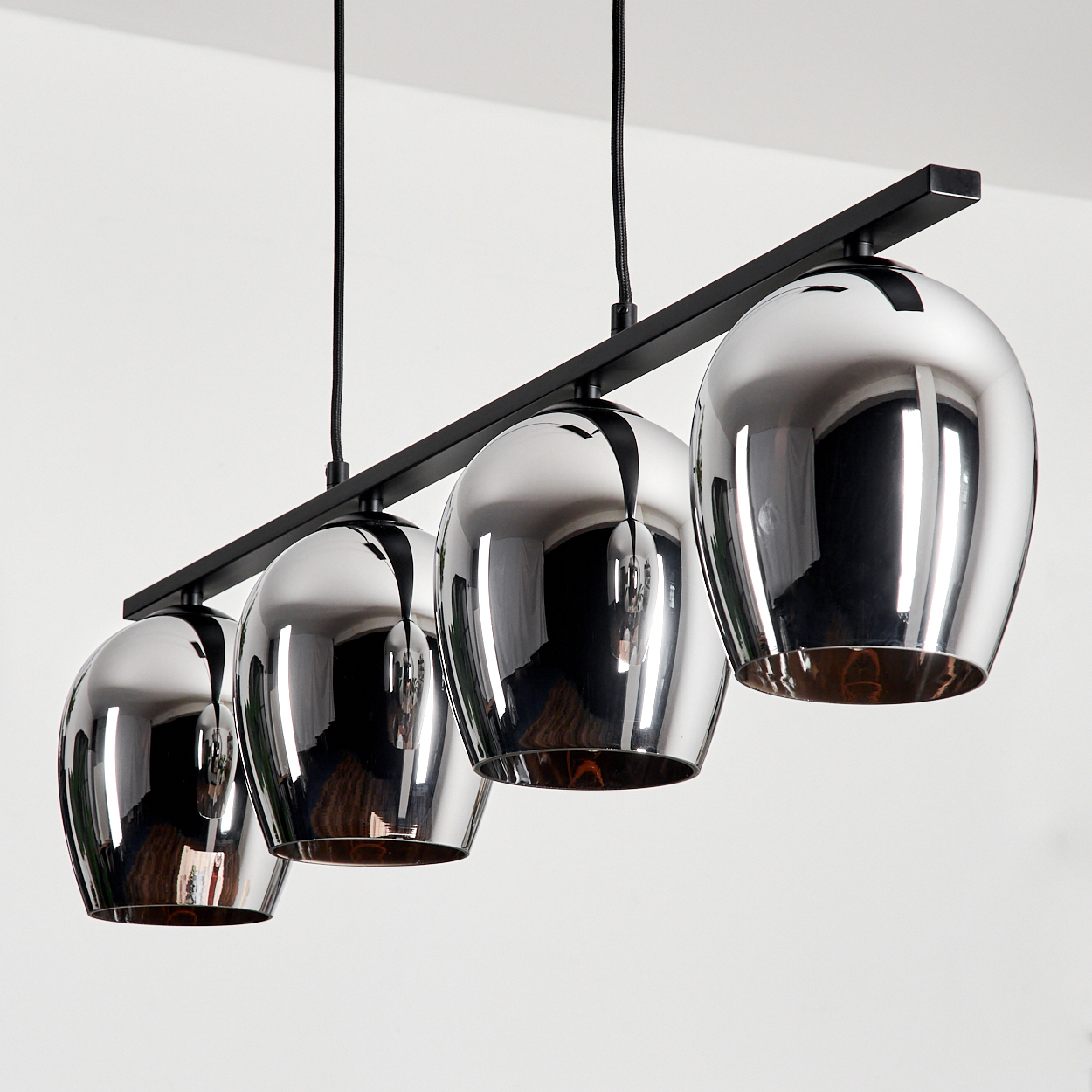 Vier kugelförmige Lampen, die von der Decke hängen. Die Lampen sind reflektierend und haben eine dunkle Oberfläche. Weißer Hintergrund.