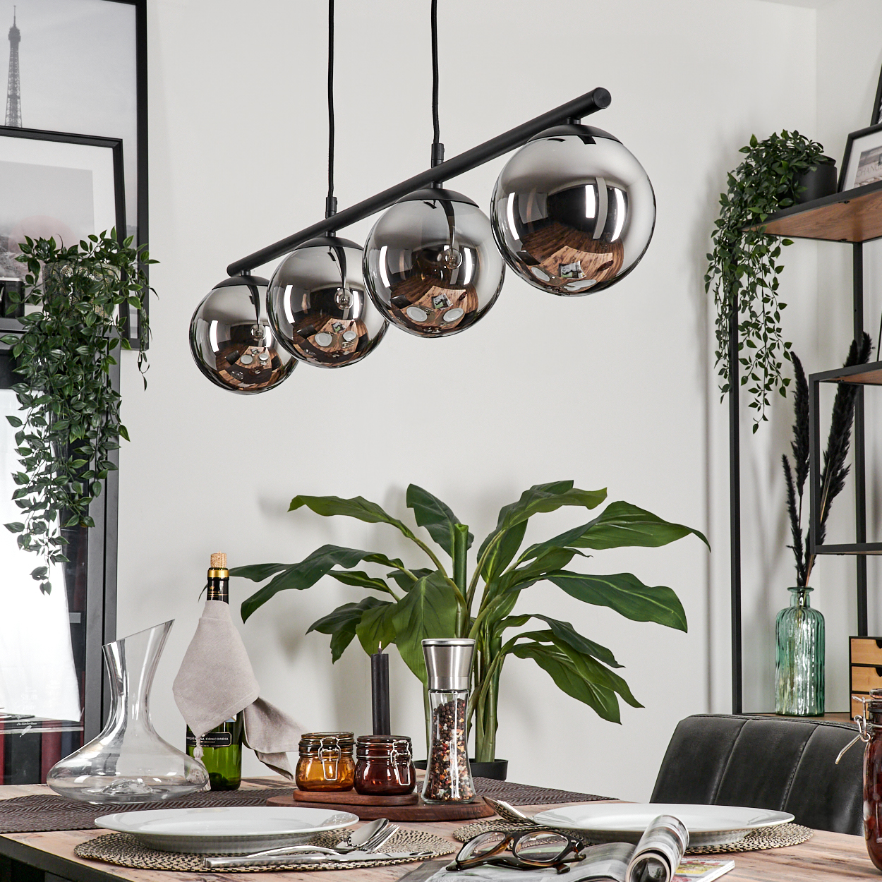 Esszimmer mit Holztisch, vier Pendelleuchten und verschiedenen Dekorationen. Die Lampen haben orangefarbene Glühbirnen.