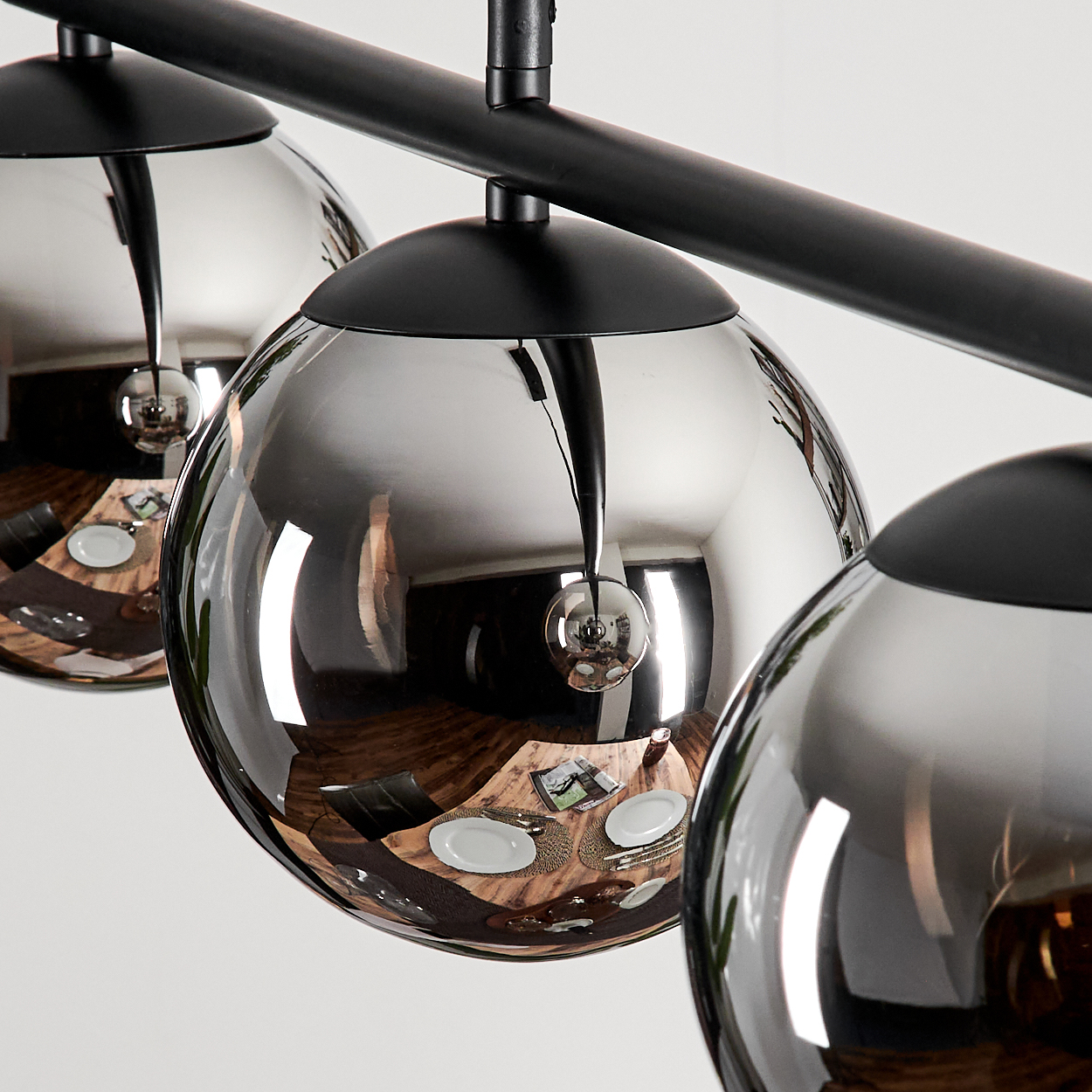 Drei verchromte Kugellampen hängen in einer Reihe. Die Lampen spiegeln eine Esstischdekoration wider. Schwarze Armaturen.