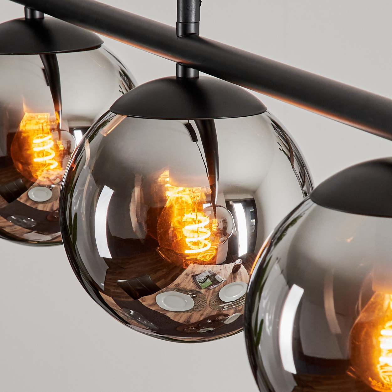 Nahaufnahme von drei kugelförmigen Lampen mit glühenden orangefarbenen Glühfäden. Die Lampen sind reflektierend und reflektieren den Raum.