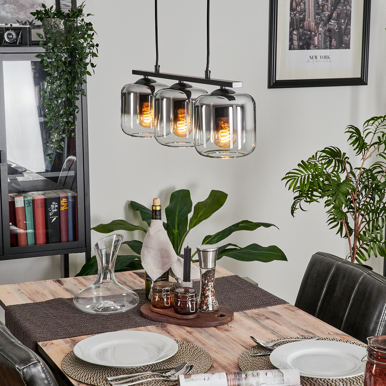 Esszimmer mit einer Hängelampe mit drei klaren Glasschirmen. Ein Tisch ist zum Abendessen gedeckt.