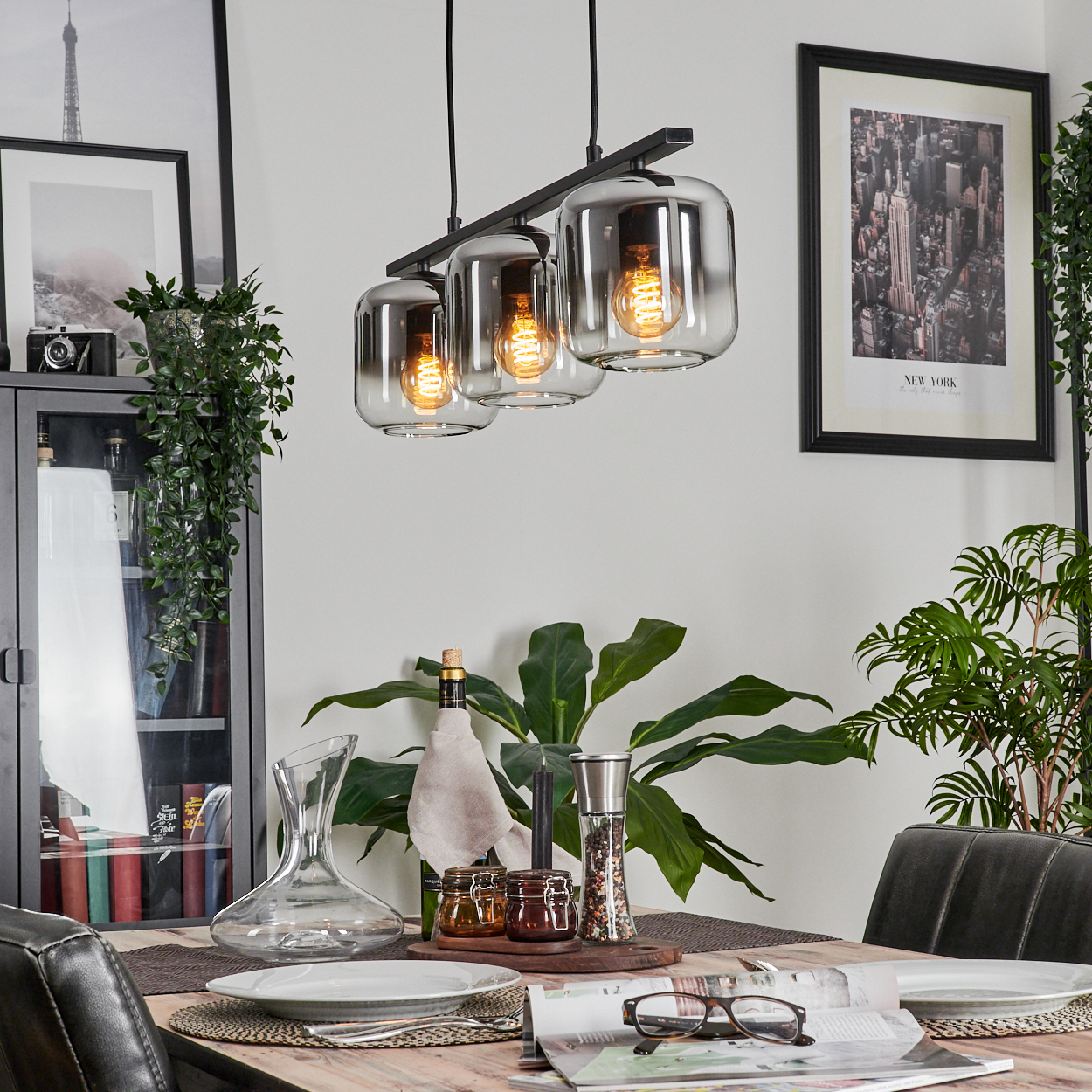 Drei Lampen mit Glühbirnen hängen über einem Esstisch mit Weindekanter, Gläsern und anderem Zubehör.