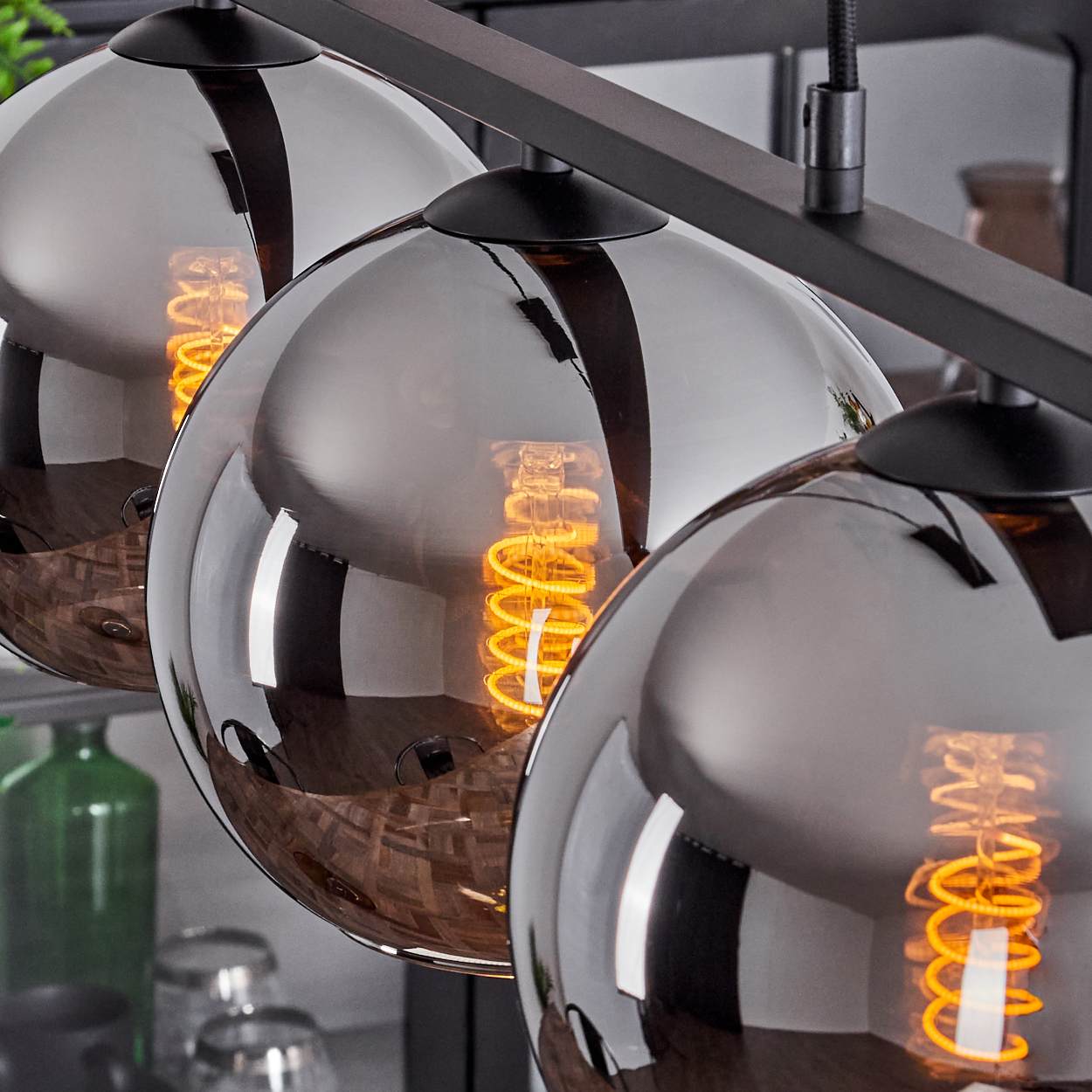 Nahaufnahme von drei Chrom-Kugel-Pendelleuchten mit Wendelglühbirnen. Die Lichter sind an.