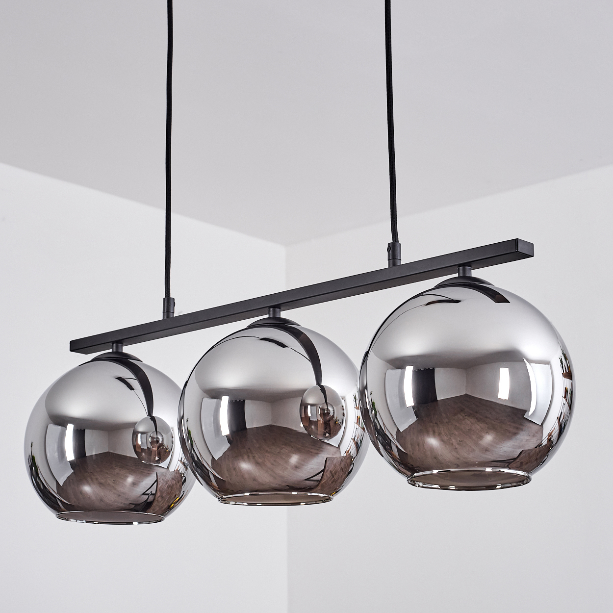 Drei silberne Kugellampen hängen von der Decke. Die Lampen spiegeln die Zimmerecken wider.
