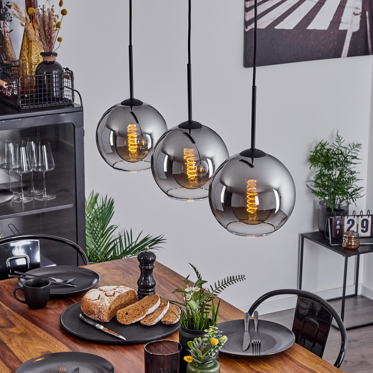 Esstisch mit drei Chrom-Kugel-Pendelleuchten darüber. Tisch ist gedeckt. Hintergrund enthält einen schwarzen Schrank.