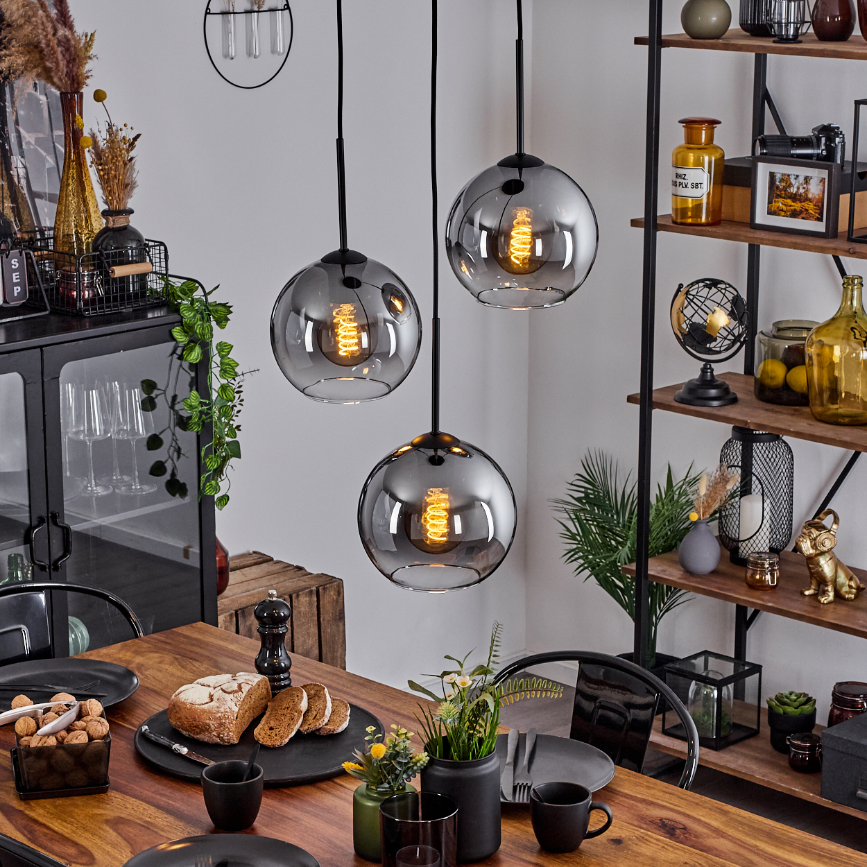 Esszimmer mit Hängelampe mit drei grauen Kugelschirmen. Ein Holztisch ist mit Dekor gedeckt.