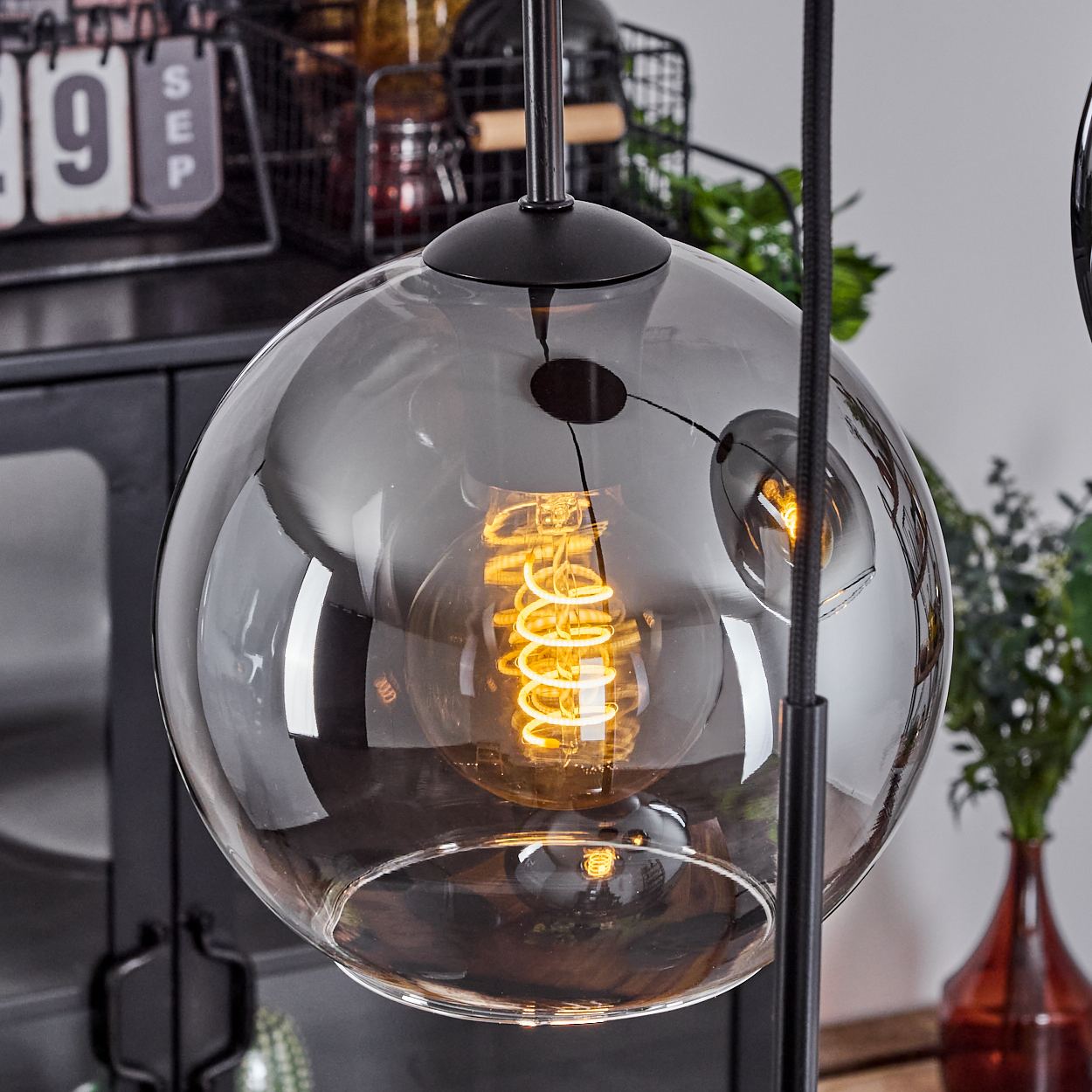 Eine Glas-Pendelleuchte mit einer leuchtenden Glühbirne. Das Licht ist rund und hat ein verspiegeltes Finish.