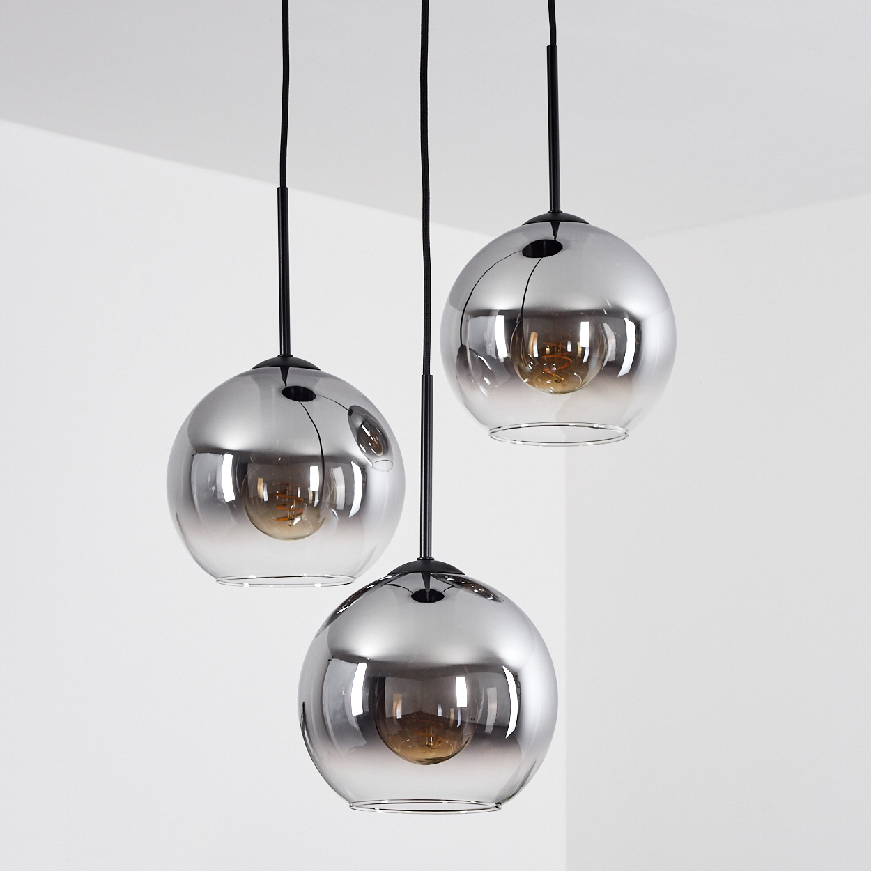 Drei Glas-Pendelleuchten mit leuchtenden Glühbirnen vor weißem Hintergrund. Die Leuchten sind kugelförmig.