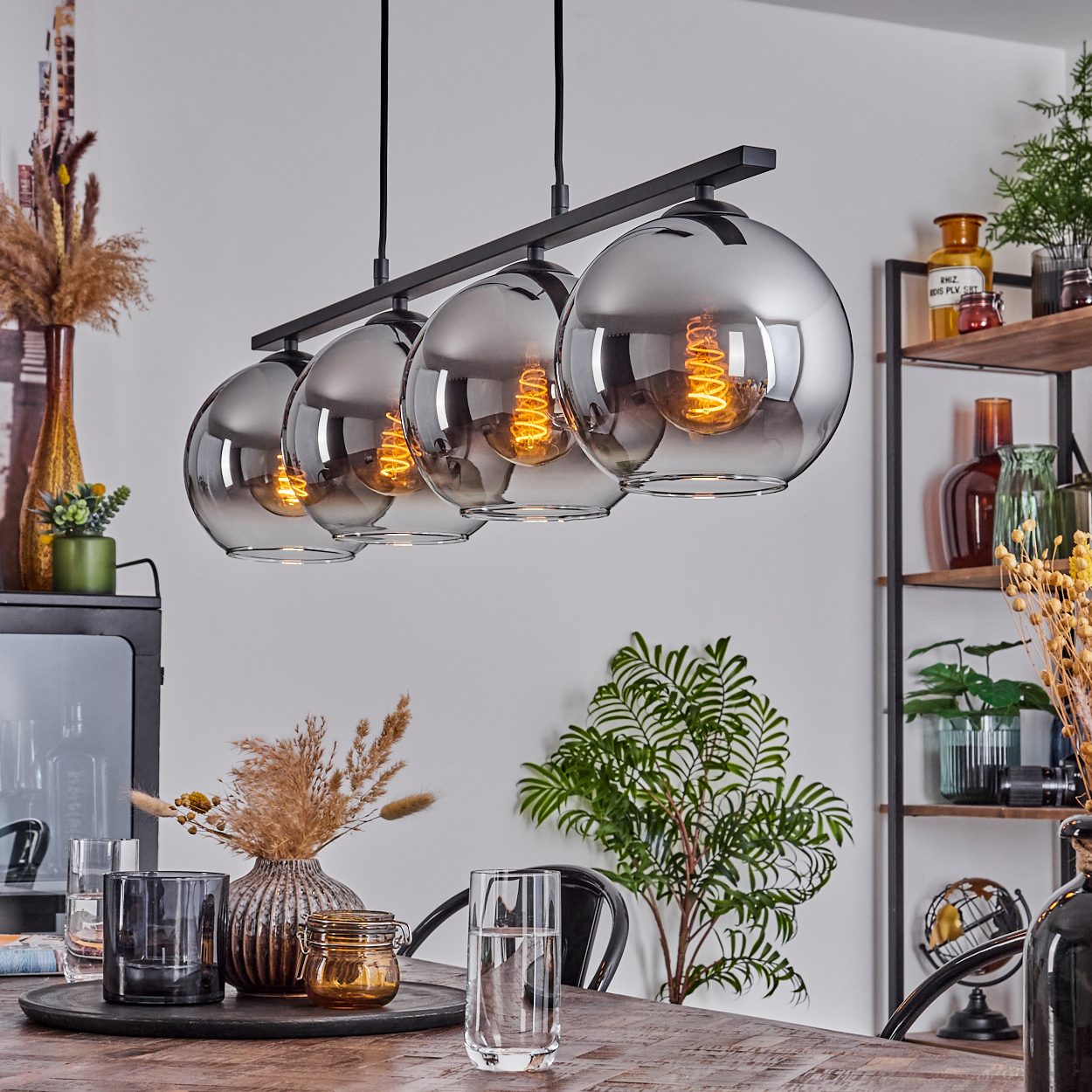 Ein Esszimmer mit Holztisch, Pendelleuchten, Pflanzen und Dekoration. Fünf Glaslampen hängen über dem Tisch.