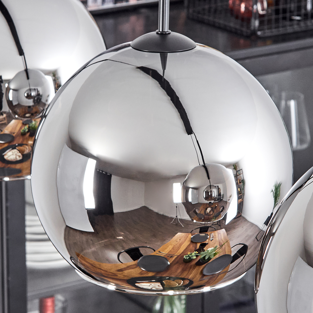 Nahaufnahme einer verchromten Pendelleuchte, die das Esszimmer und den Tisch reflektiert. Andere Lichter unscharf.
