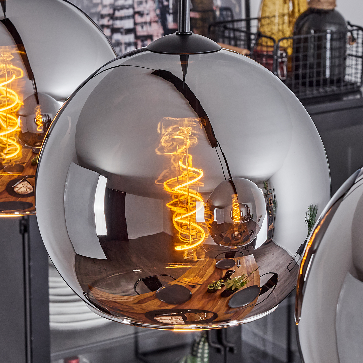 Nahaufnahme einer verchromten Pendelleuchte mit einer Wendelglühbirne, die das Esszimmer reflektiert. Andere Lichter unscharf.