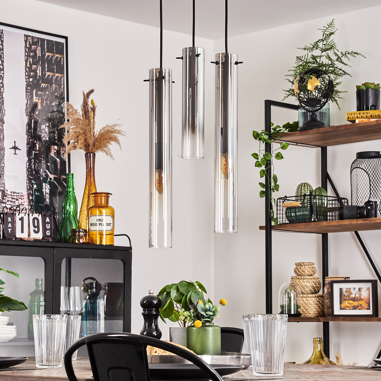 Ein Esszimmer mit Holztisch, drei Pendelleuchten, Pflanzen und Regalen voller Gegenstände.