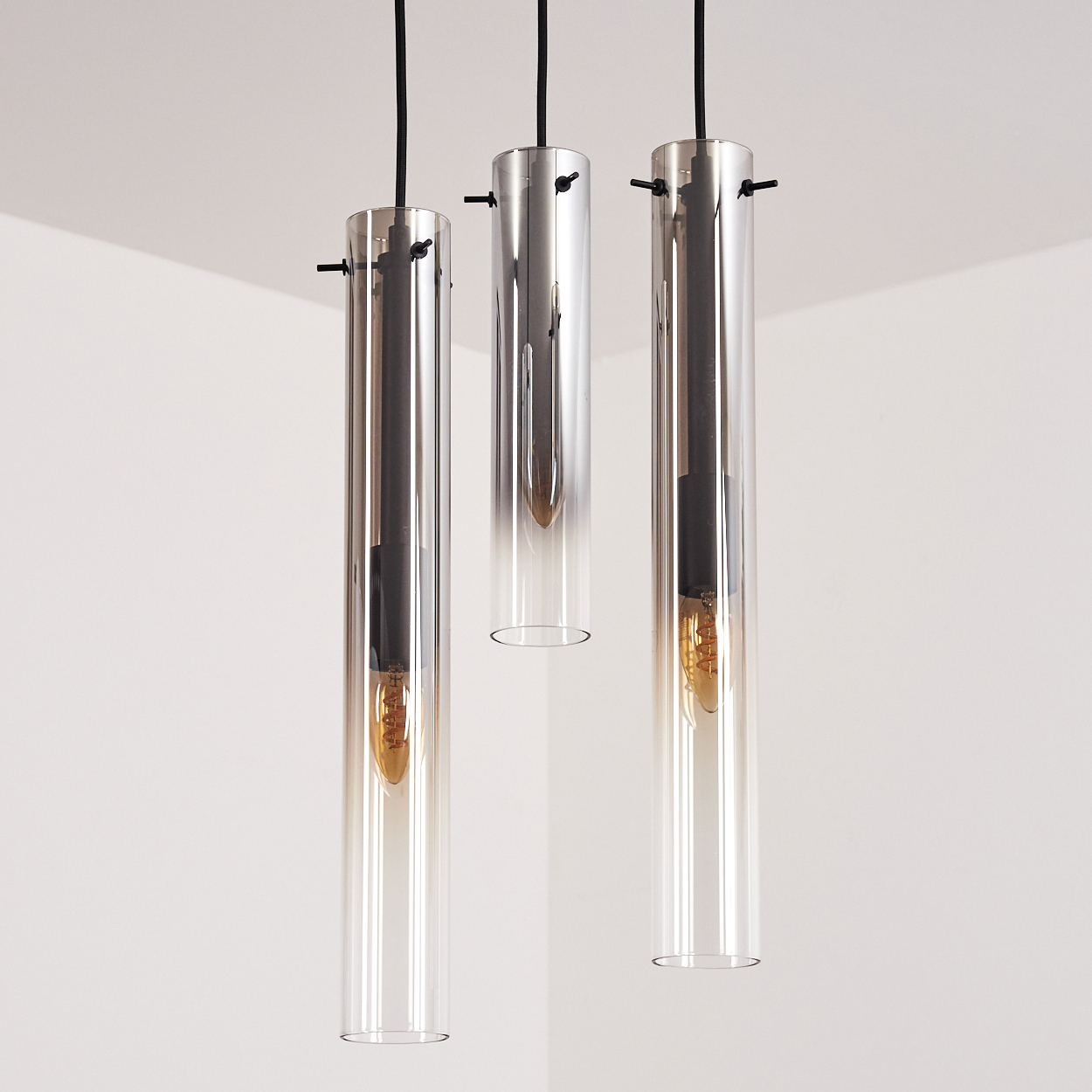 Drei Pendelleuchten mit zylindrischen Glasschirmen hängen von der Decke. Die Glühbirnen im Inneren sind sichtbar.