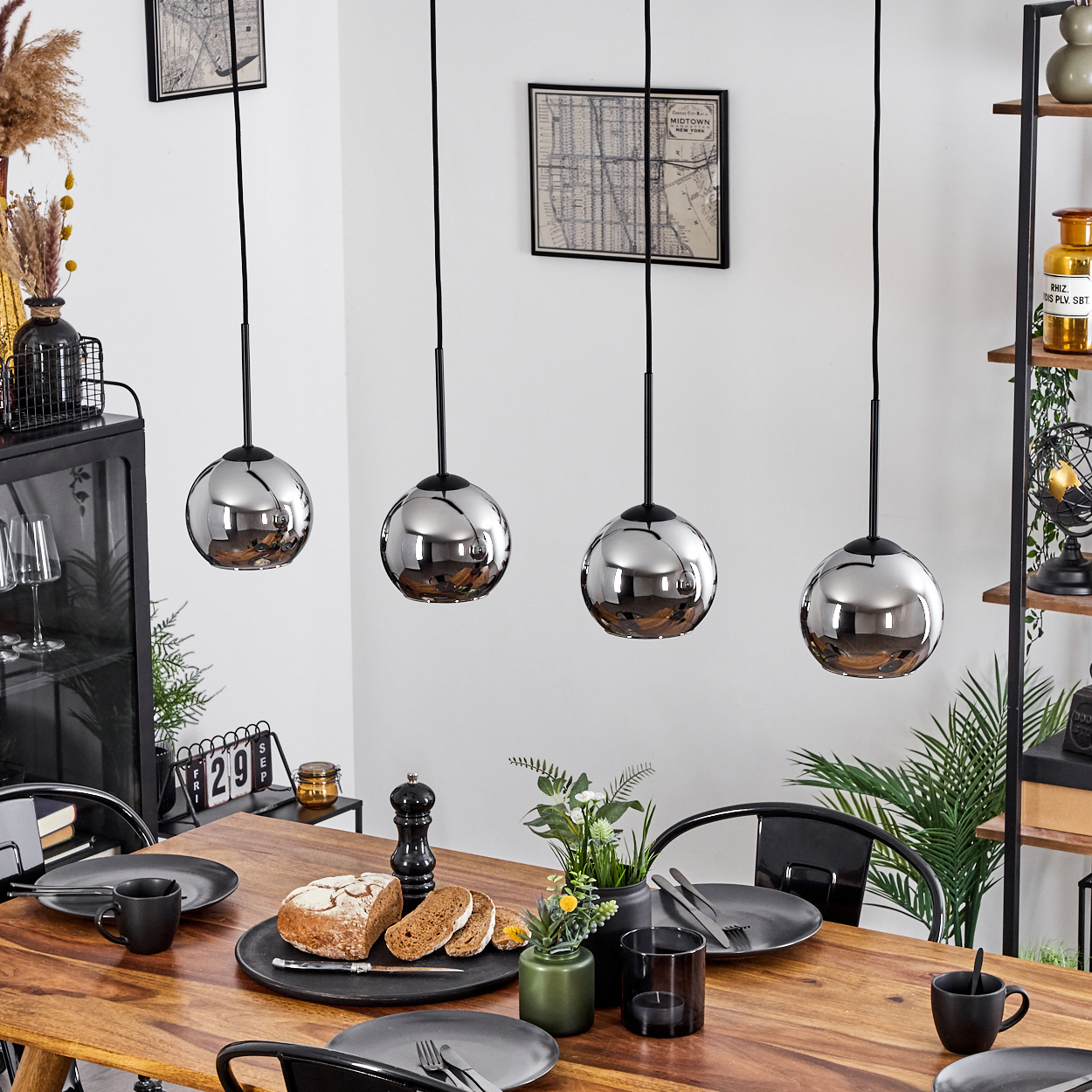 Esszimmer mit Holztisch, schwarzem Teller und vier Pendelleuchten mit silbernen Schirmen.