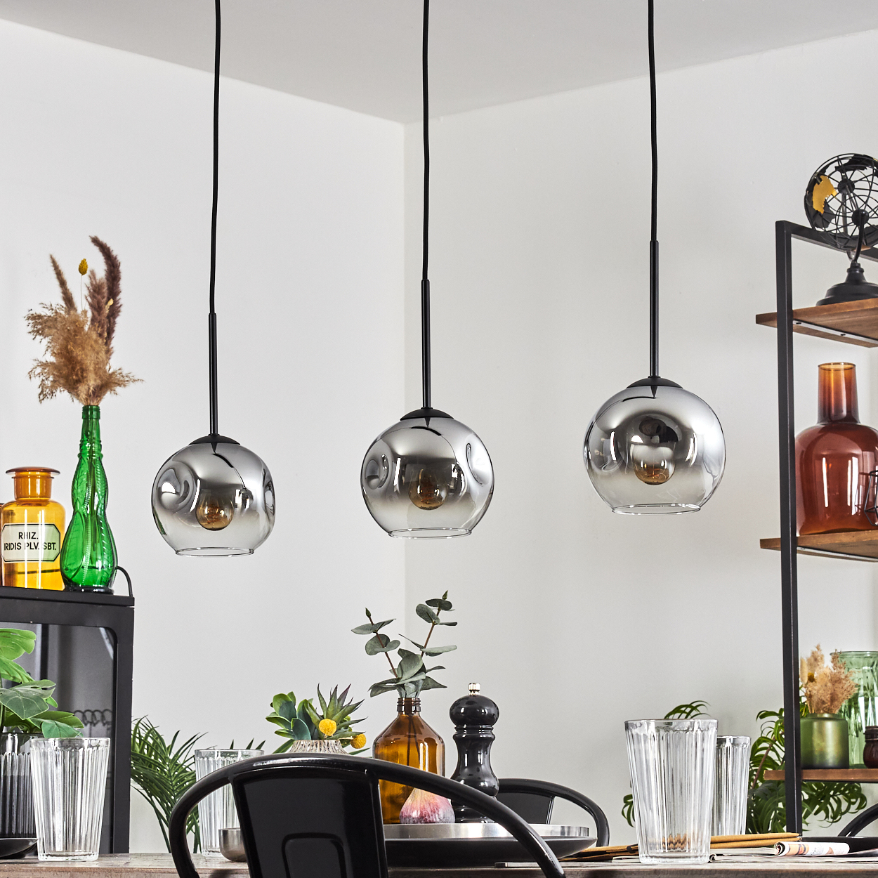 Drei Glaspendelleuchten hängen über einem Esstisch mit Tellern und Gläsern in einem stilvollen Esszimmer.