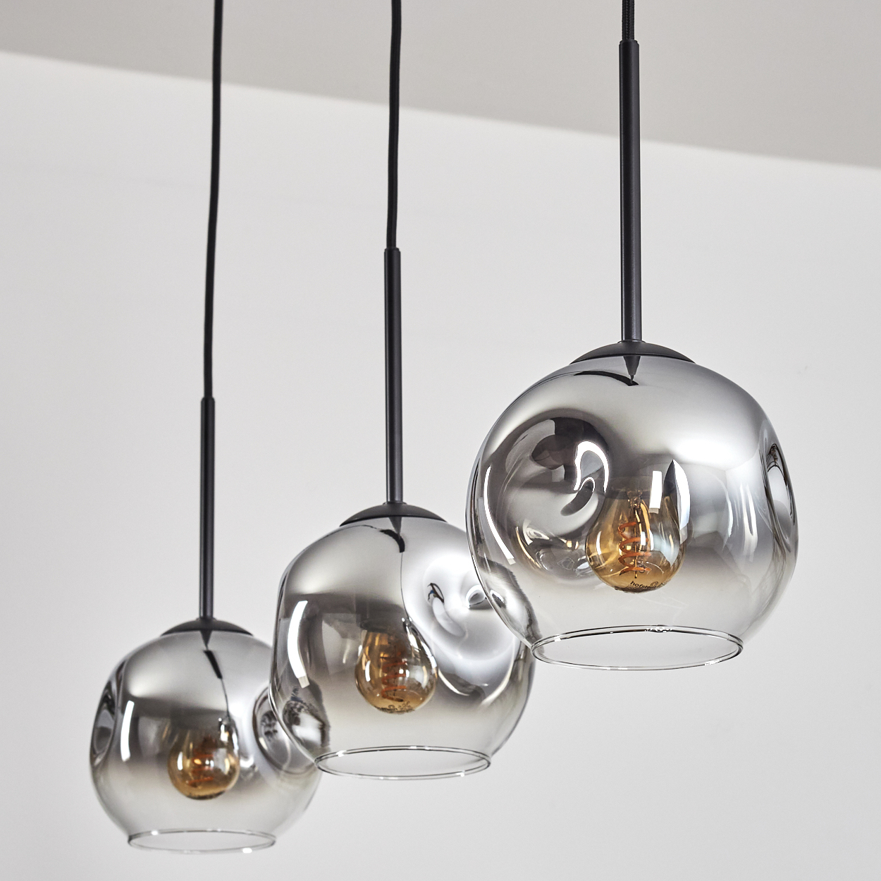 Drei silberne Pendelleuchten mit sichtbaren Glühbirnen. Die Lichter hängen mit weißem Hintergrund.