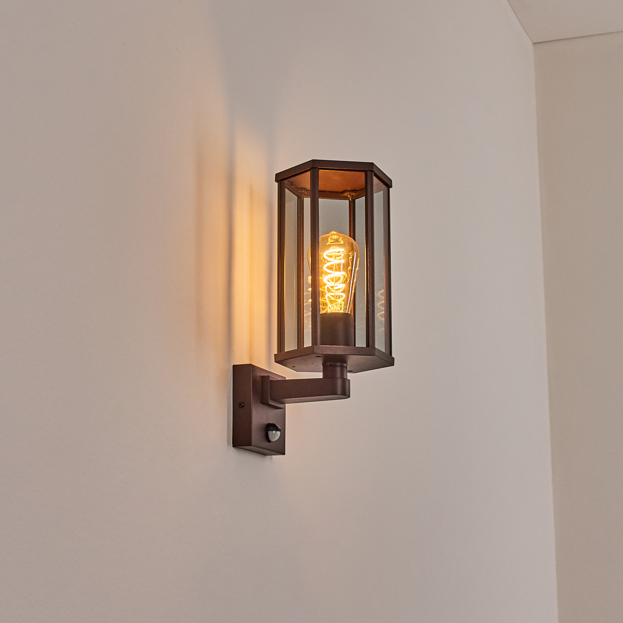 Eine Wandleuchte mit Glasgehäuse und freiliegender Glühbirne, an einer hellbeigen Wand angebracht.