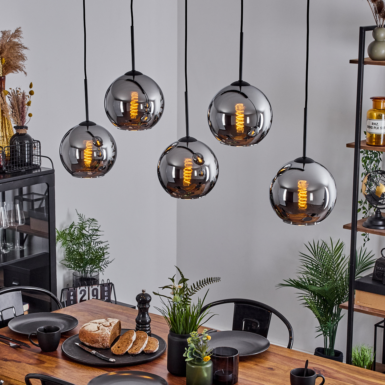Esszimmer mit Holztisch und hängenden Kugelleuchten. Die Leuchten haben silberne Kugeln mit sichtbaren Glühbirnen.