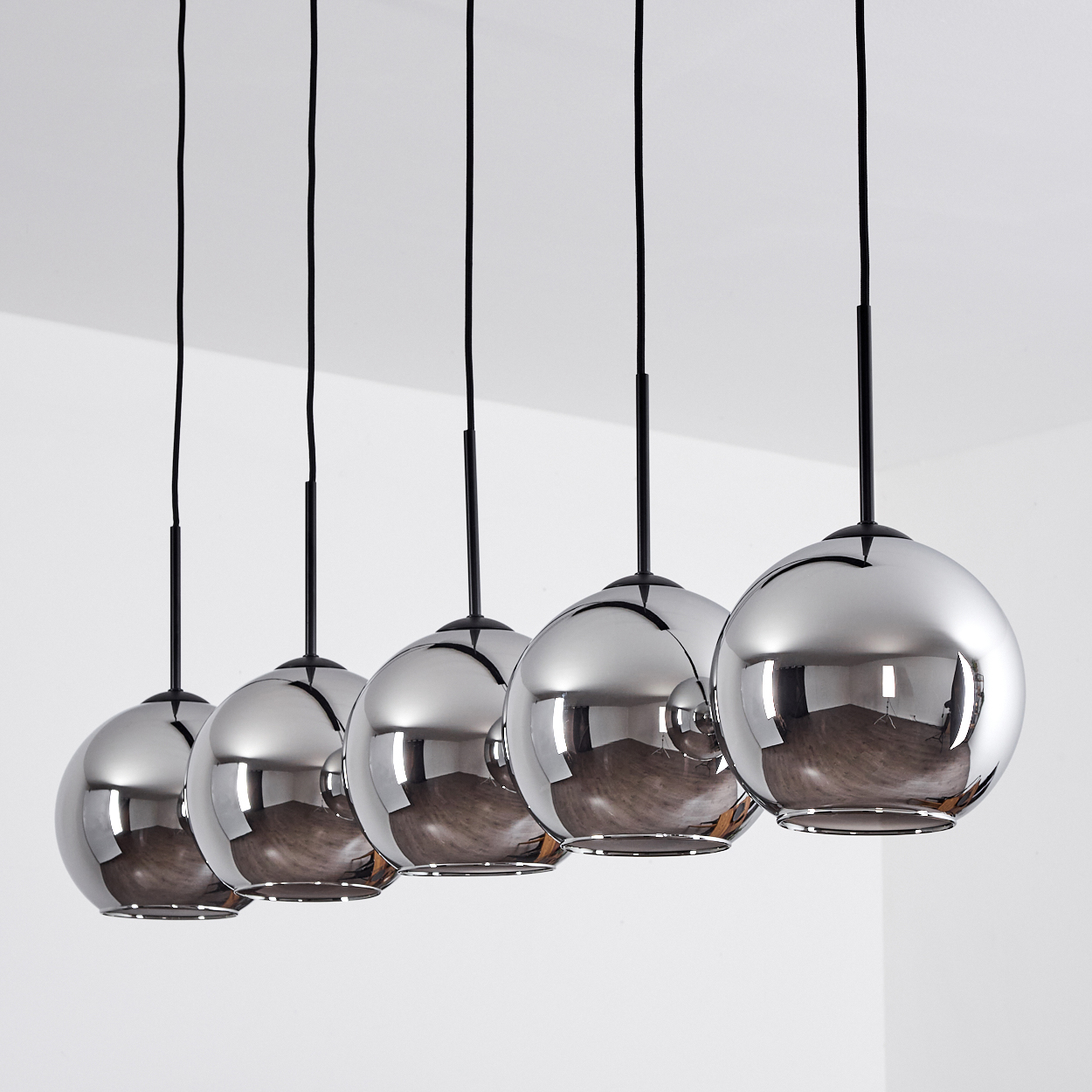 Fünf verchromte, kugelförmige Pendelleuchten hängen von der Decke, jede mit schwarzem Kabel.