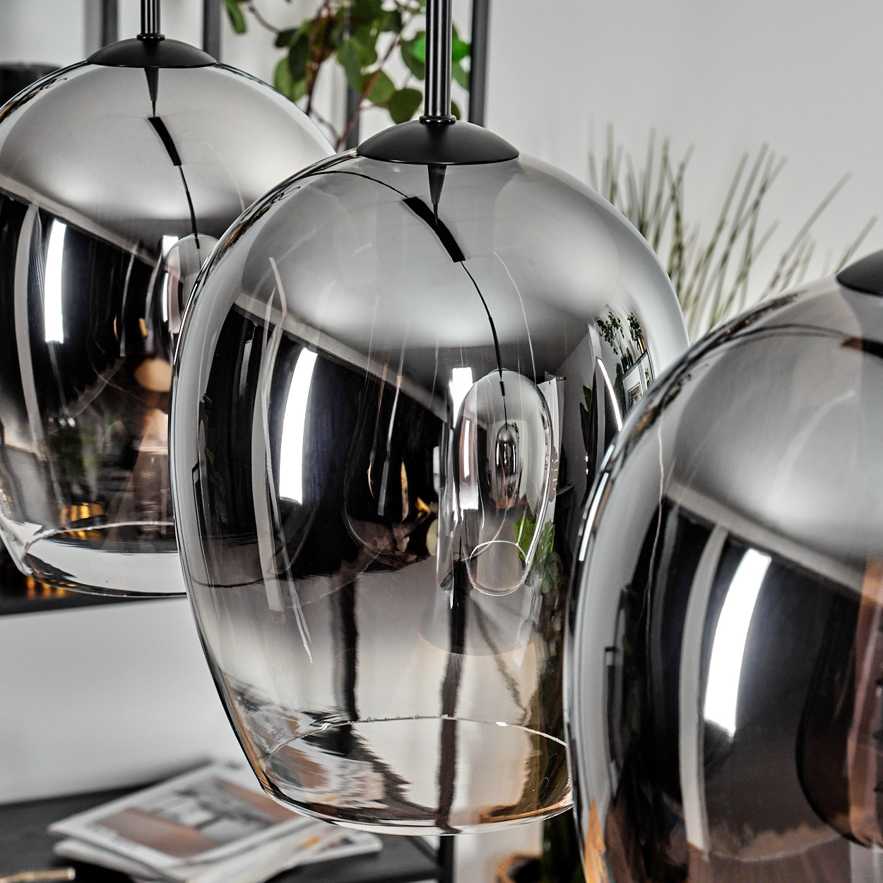 Nahaufnahme von drei modernen Pendelleuchten mit klaren und silbernen Farbverlaufsglasschirmen, schwarzes Finish.