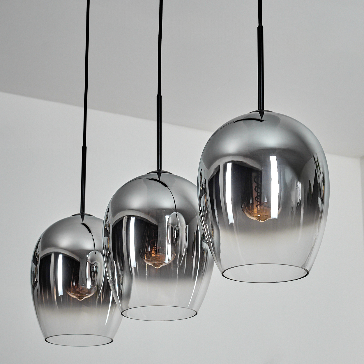 Drei silberne Pendelleuchten mit sichtbaren Glühbirnen, die von der Decke hängen.