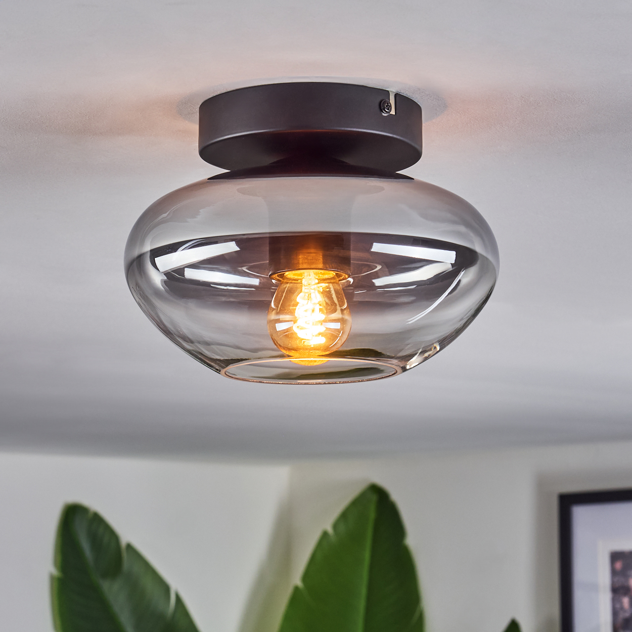 Deckenleuchte mit schwarzem Sockel und klarem, abgerundetem Glasschirm. Das Licht ist an.