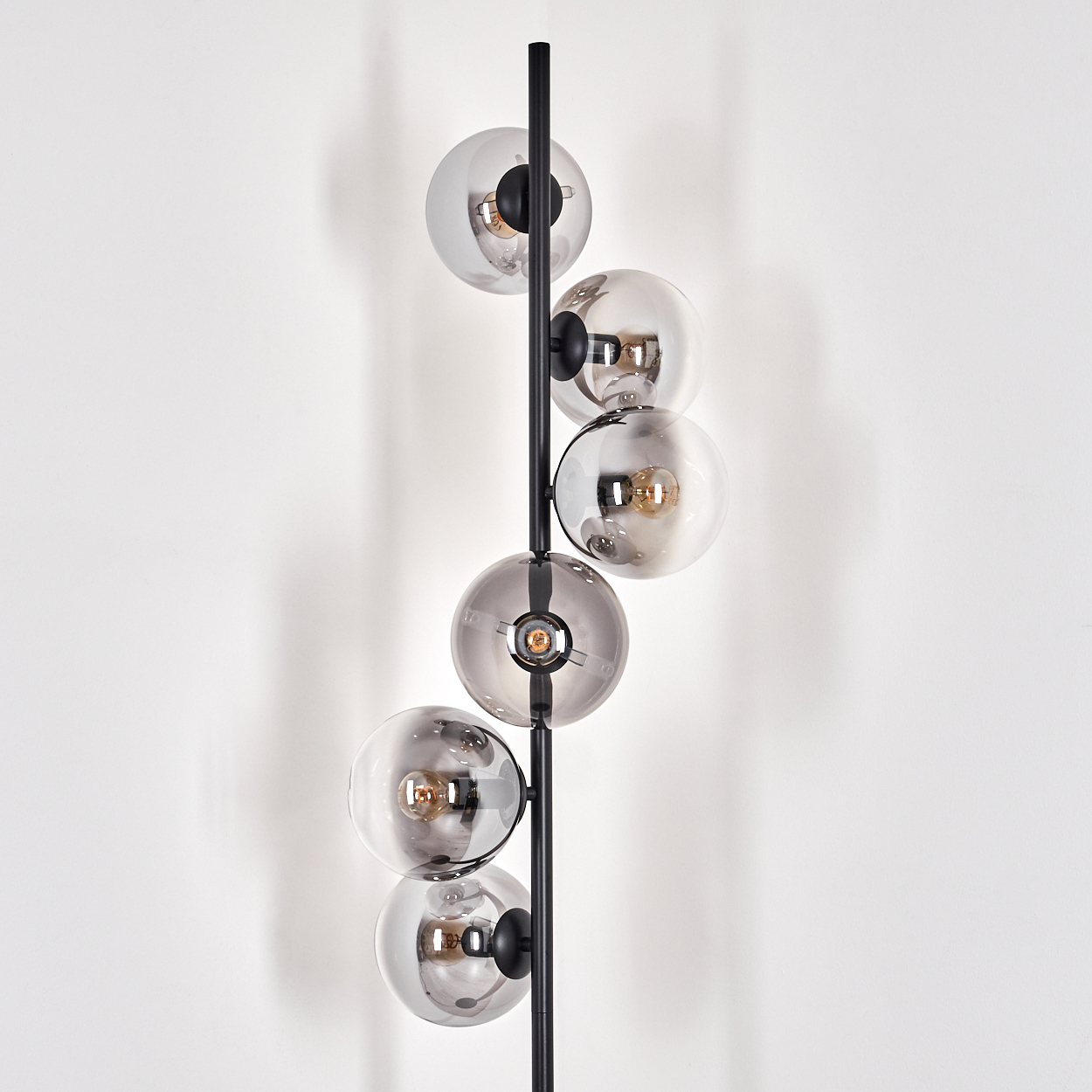 Eine schwarze Stehlampe mit sechs rauchfarbenen Glaskugeln. Die Kugeln sind vertikal an einem schwarzen Metallpfahl angeordnet, mit Glühbirnen darin.