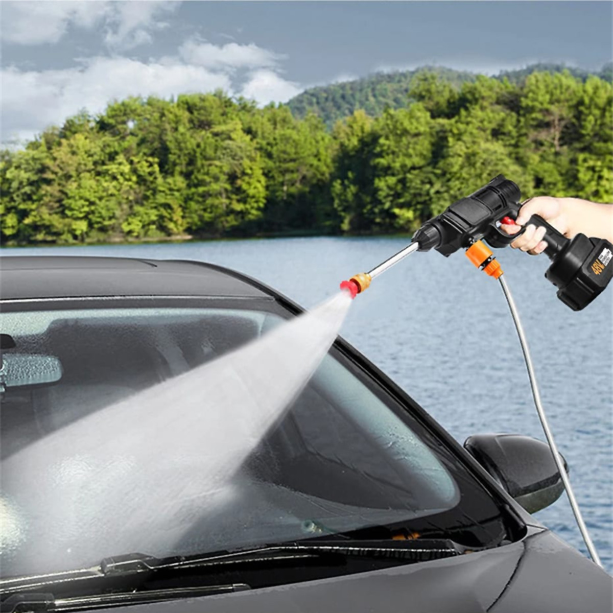 Un coche siendo lavado con una hidrolavadora. El agua sale a chorros de la boquilla. Fondo de naturaleza.