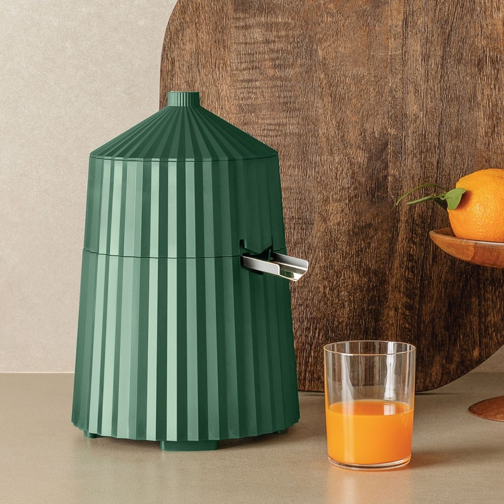 Spremiagrumi verde con un bicchiere di succo d'arancia e un tagliere in legno sullo sfondo. Un'arancia è su un supporto in legno.