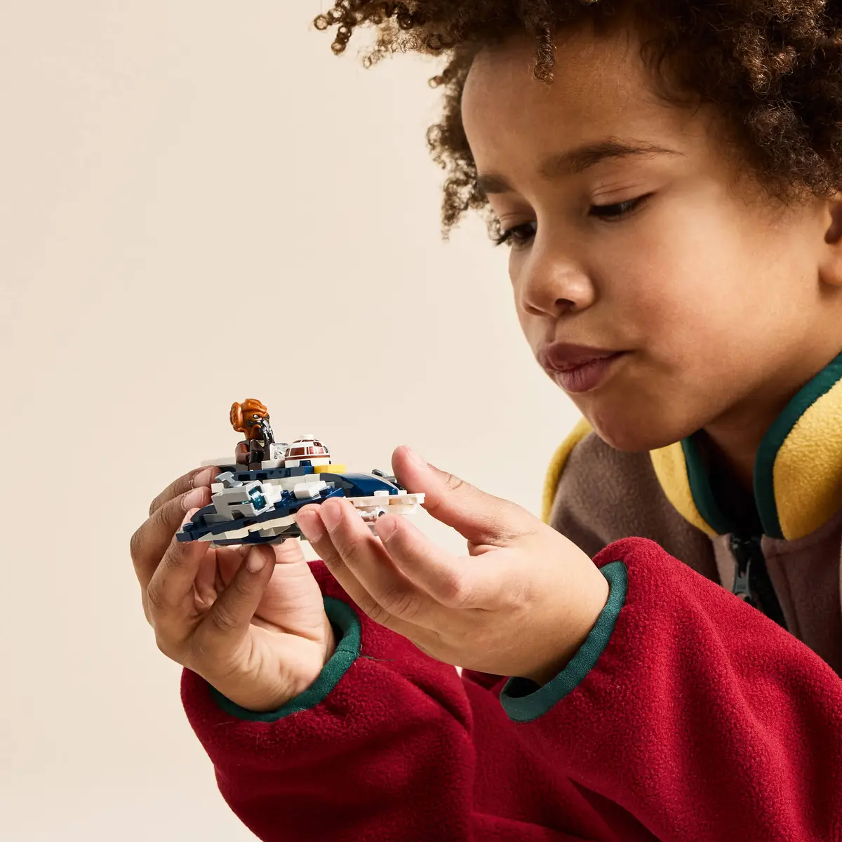 Dziecko trzyma mały statek kosmiczny Lego. Statek kosmiczny jest niebiesko-biały.