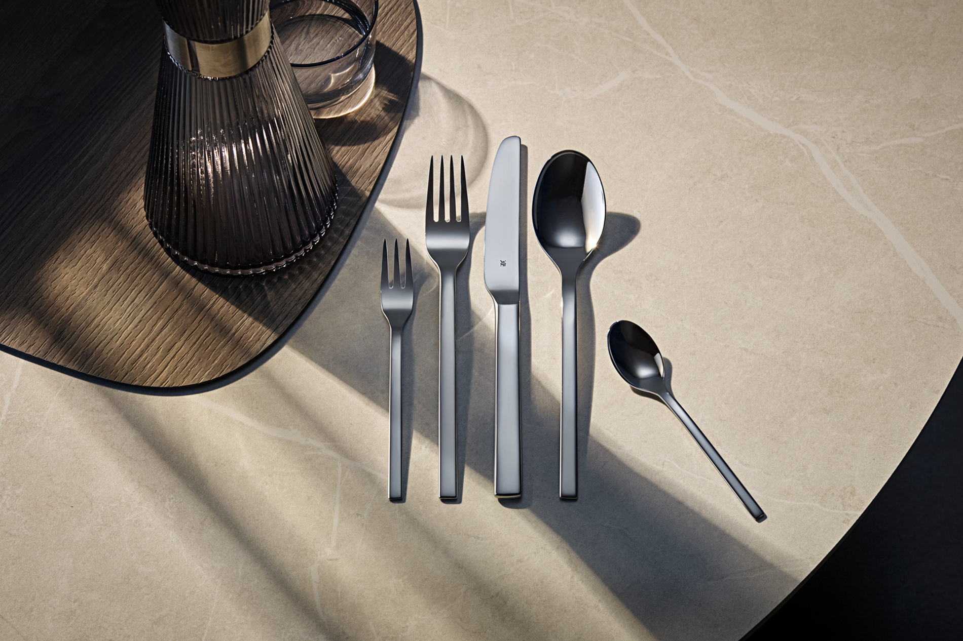 Set di posate su un tavolo di marmo. Include forchette, coltello e cucchiai. L'illuminazione crea ombre.