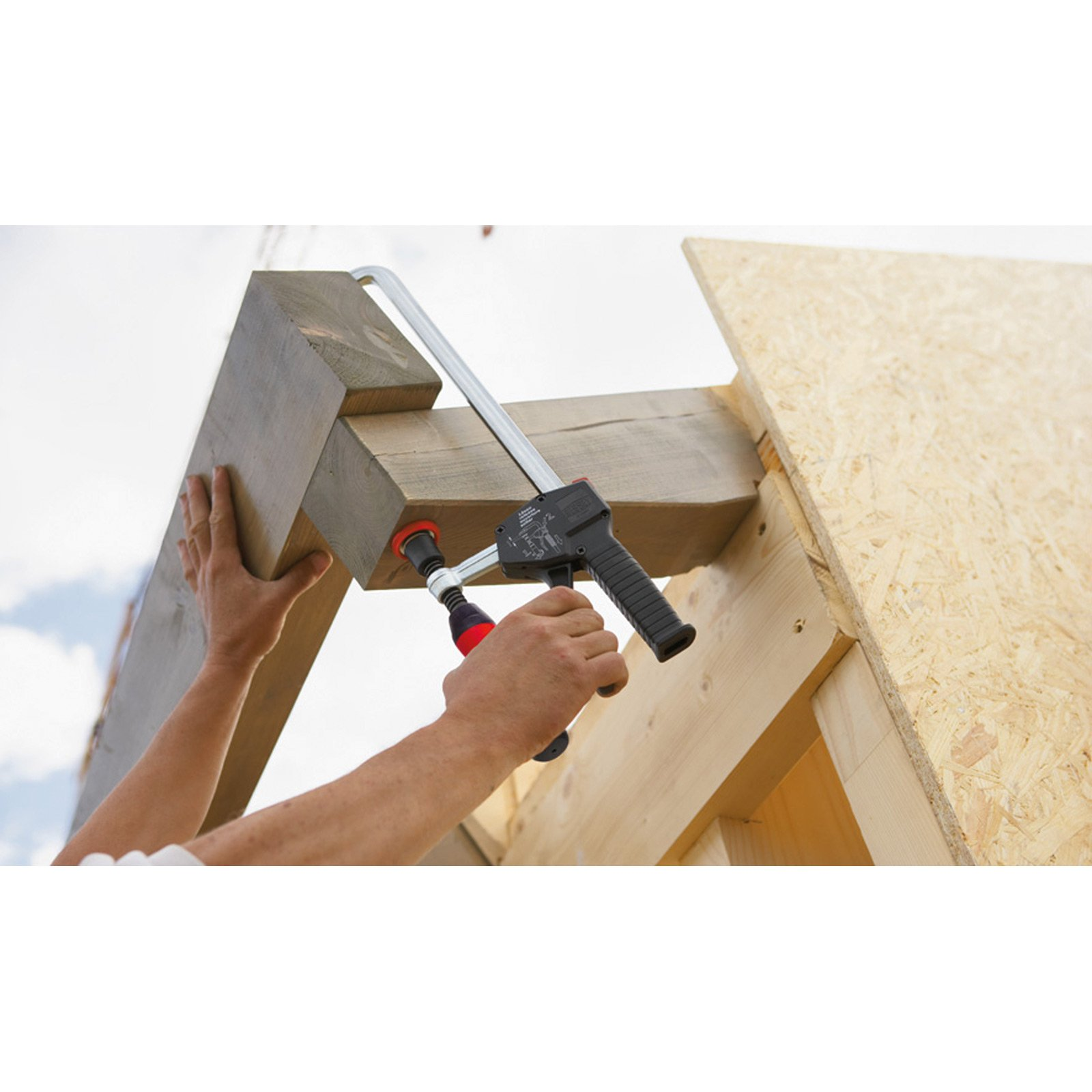 Ręce zaciskają drewniane belki pod częściowo pochmurnym niebem. Plac budowy z nowym drewnem.