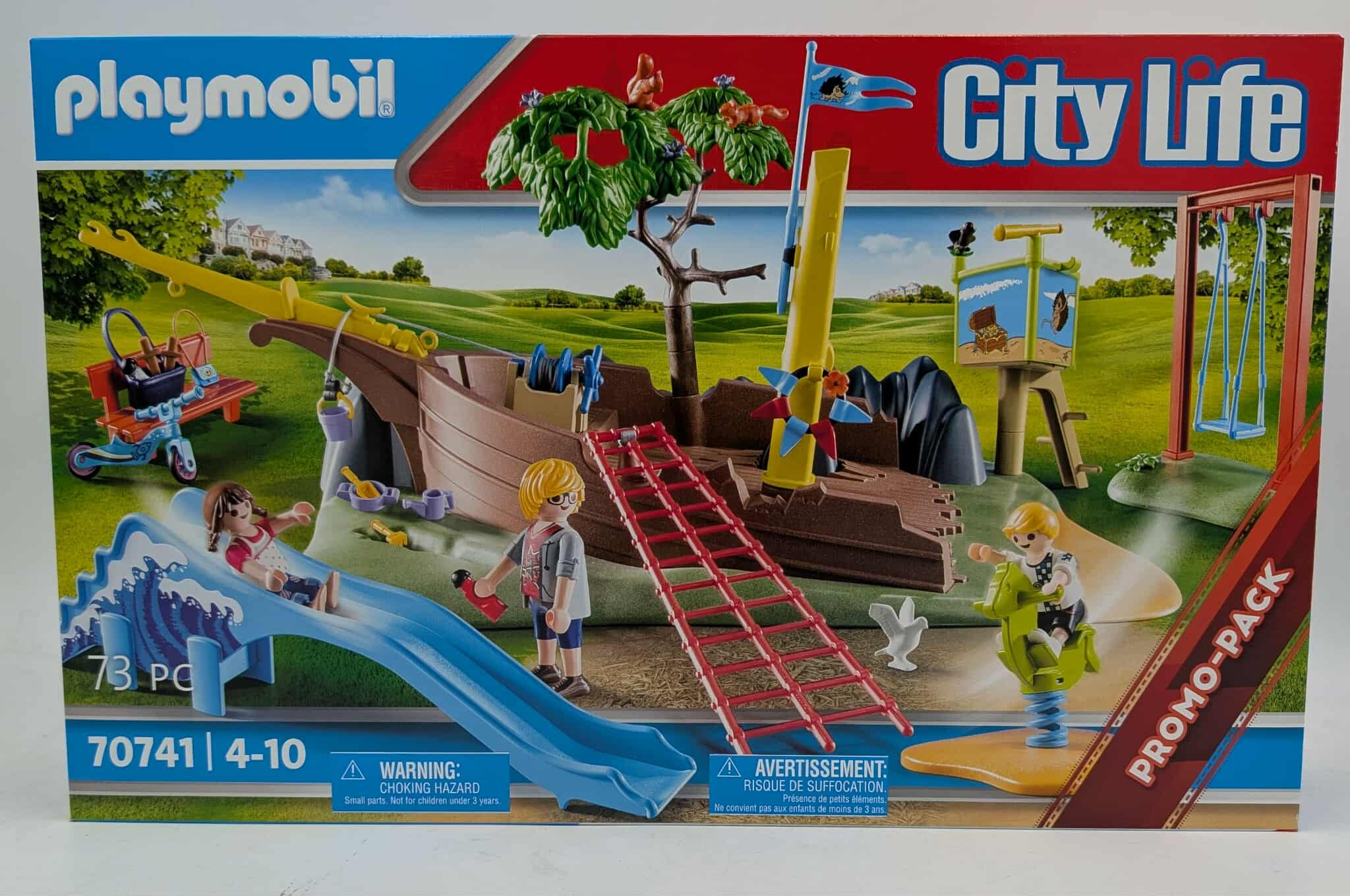 Playmobil City Life Box-Set mit einem Spielplatz mit Rutsche, Schiff und Figuren. Grünes Gras und blauer Himmel.