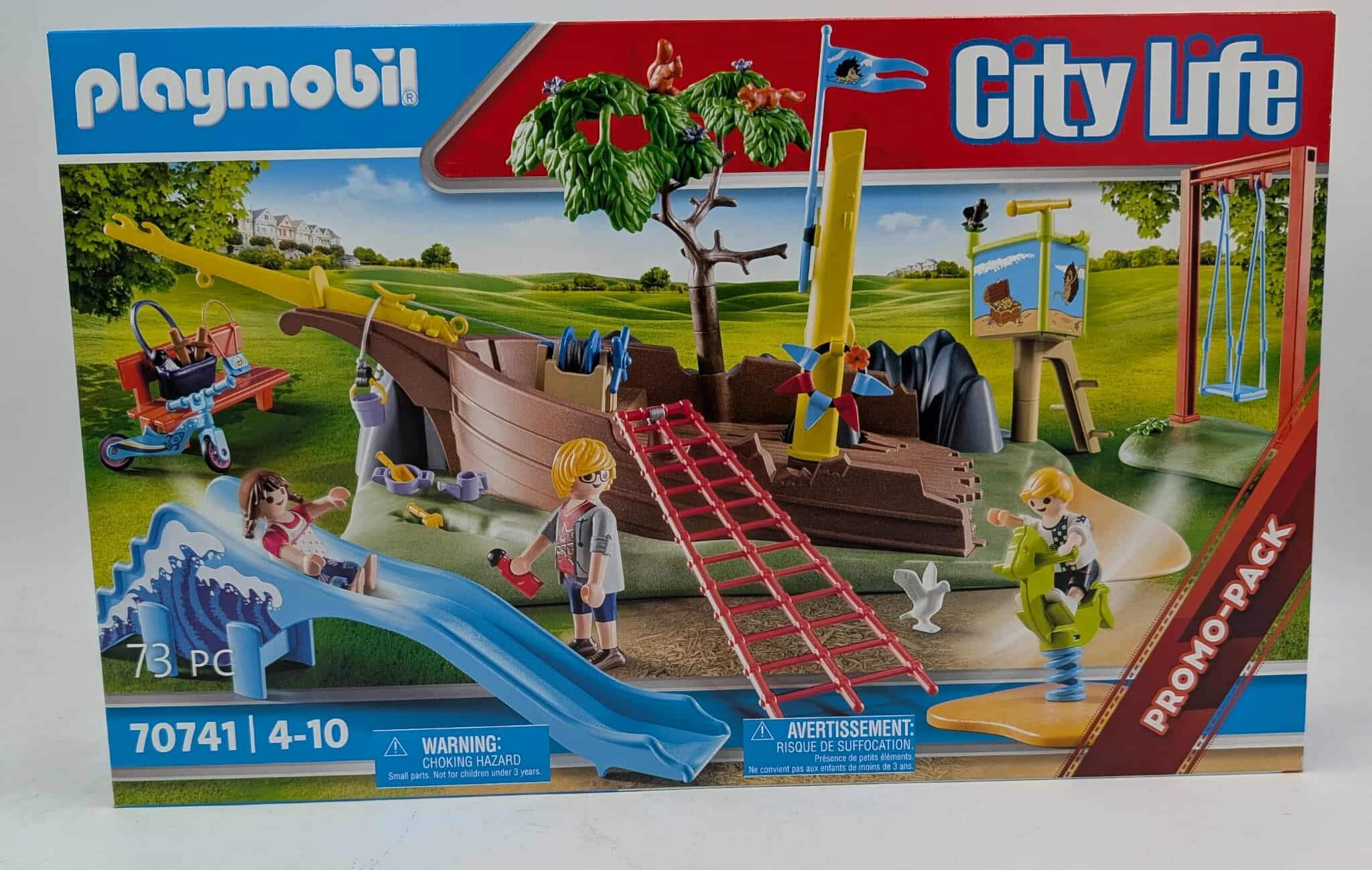 Playmobil City Life Box mit einem Spielplatz mit Rutsche, Schiff und Figuren. Grünes Gras und blauer Himmel.