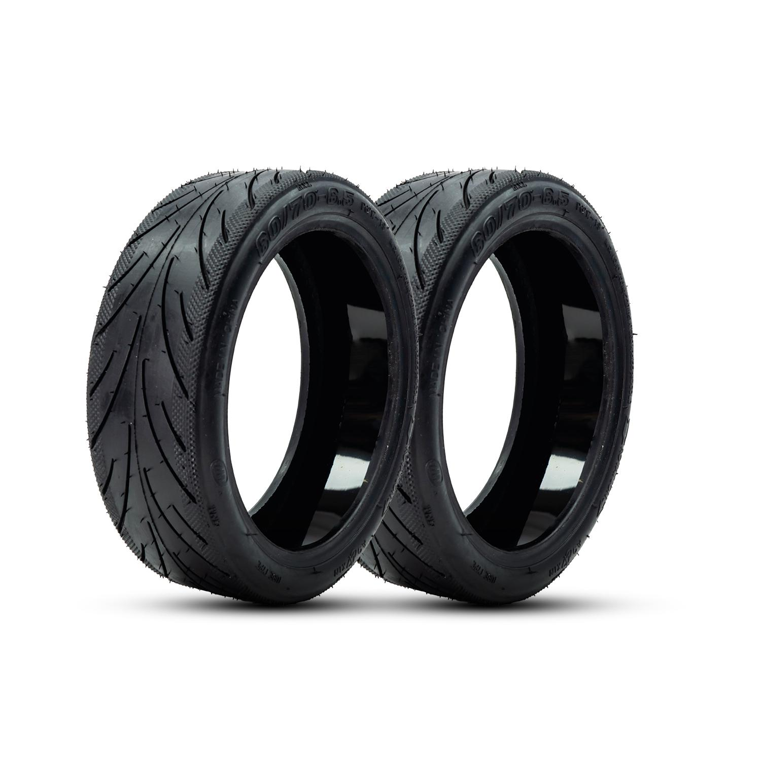 Dos neumáticos negros de motocicleta, uno al lado del otro, sobre un fondo blanco. Los neumáticos tienen dibujo.
