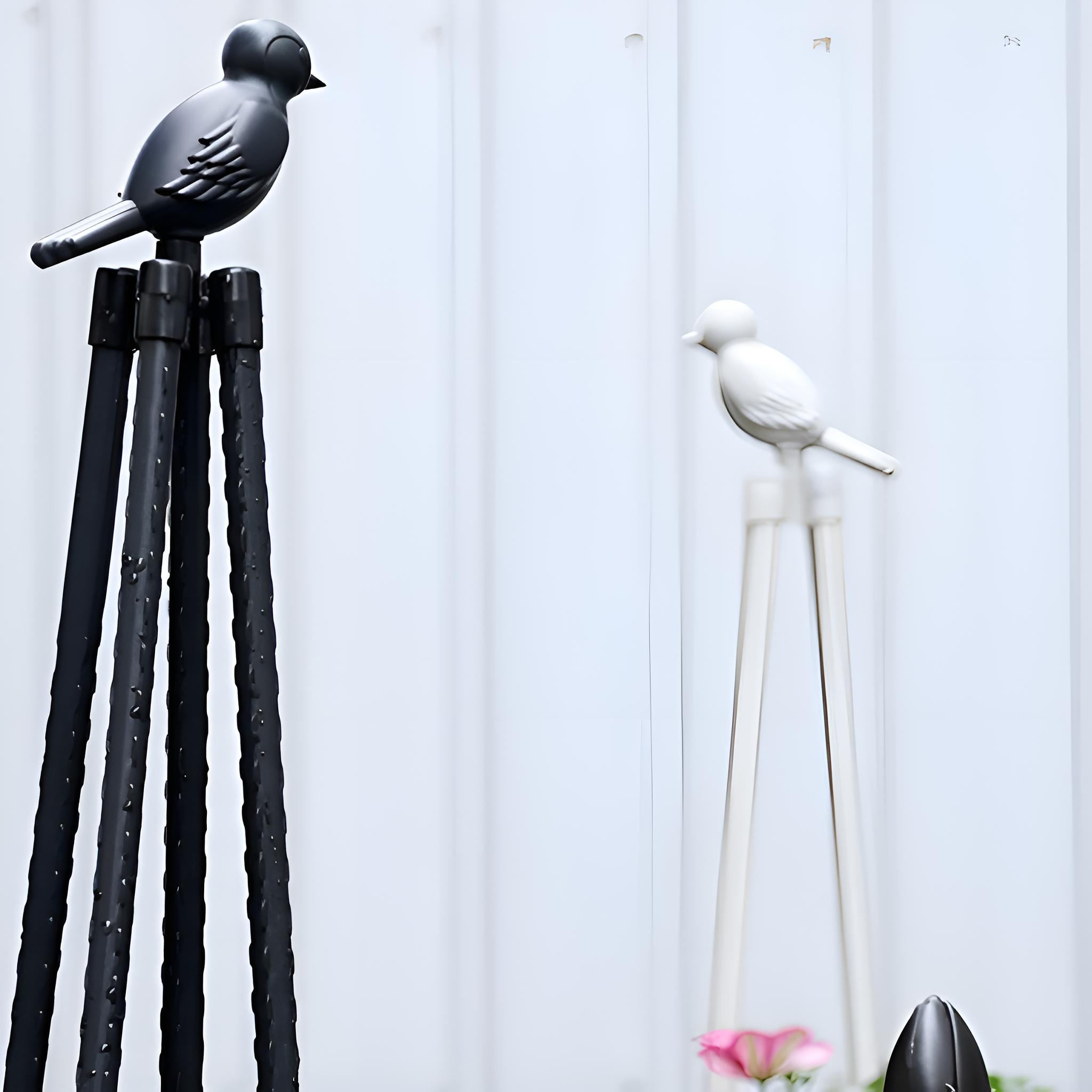 Zwei dekorative Vogelstatuen auf Stangen. Eine schwarz, eine weiß. Beide haben lange Beine. Weißer Hintergrund, Licht dahinter.