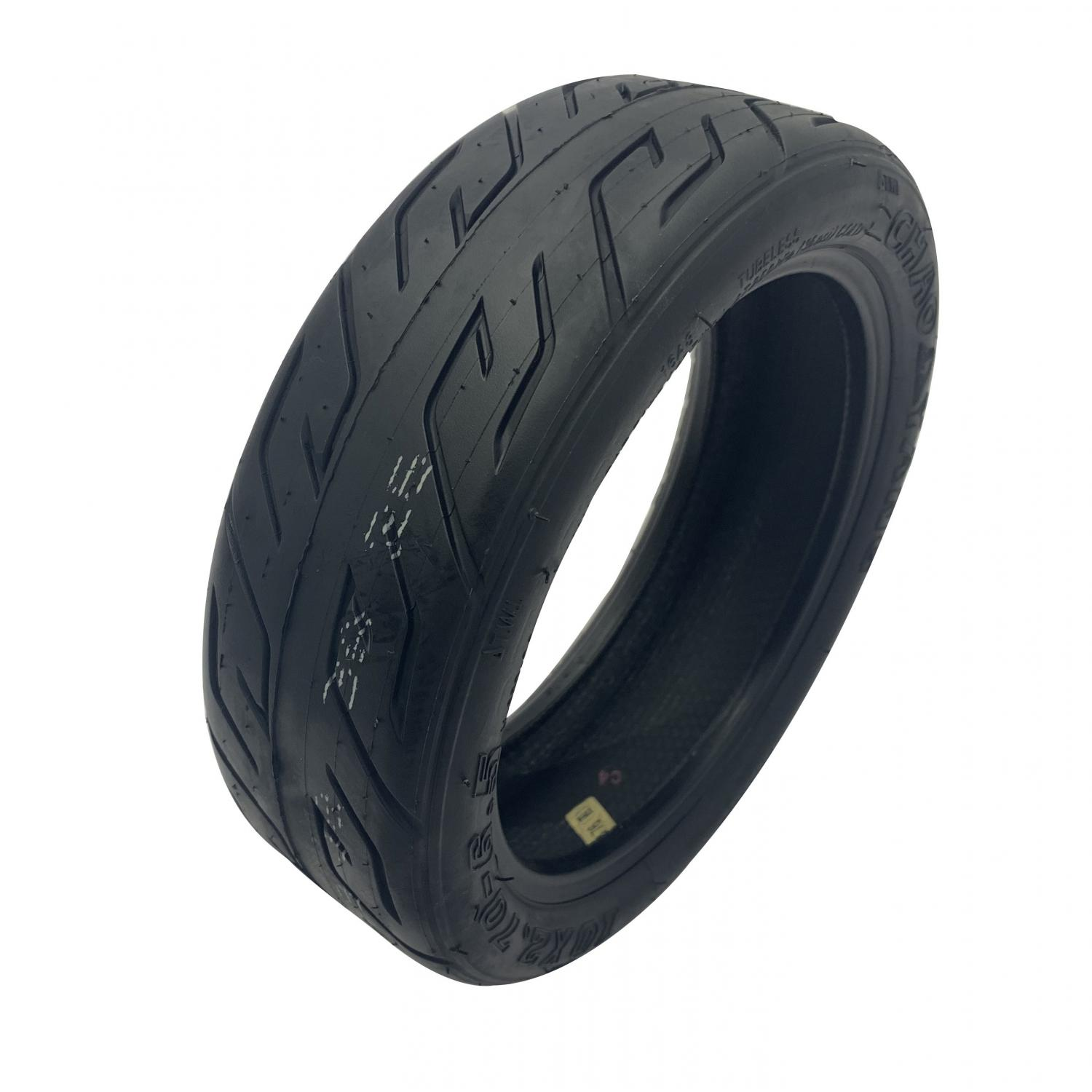 Un neumático negro de scooter, en ángulo, con un dibujo de la banda de rodadura y marcas de texto blancas.