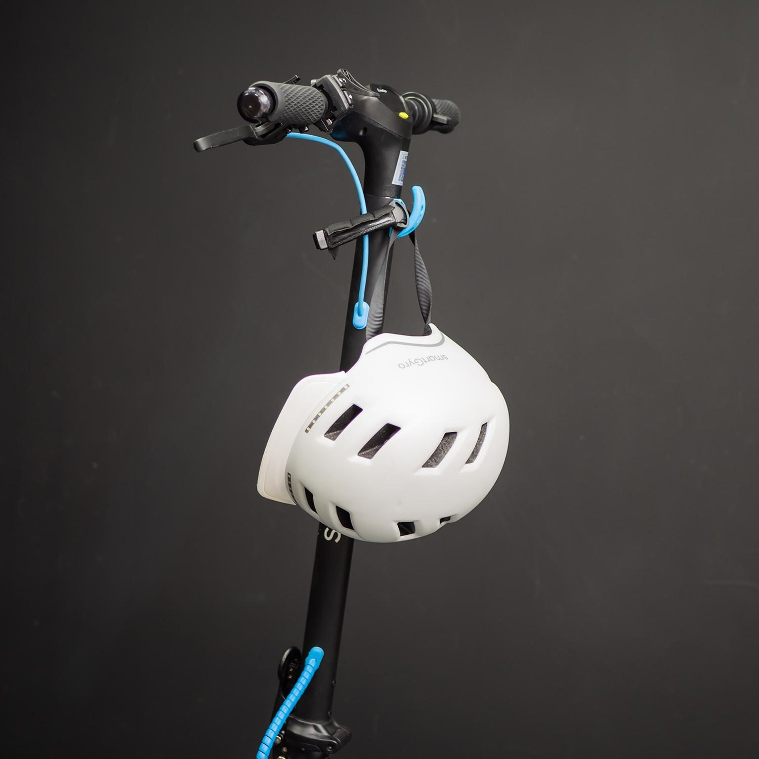 Casco blanco colgado de un patinete negro. El patinete está sobre un fondo negro.