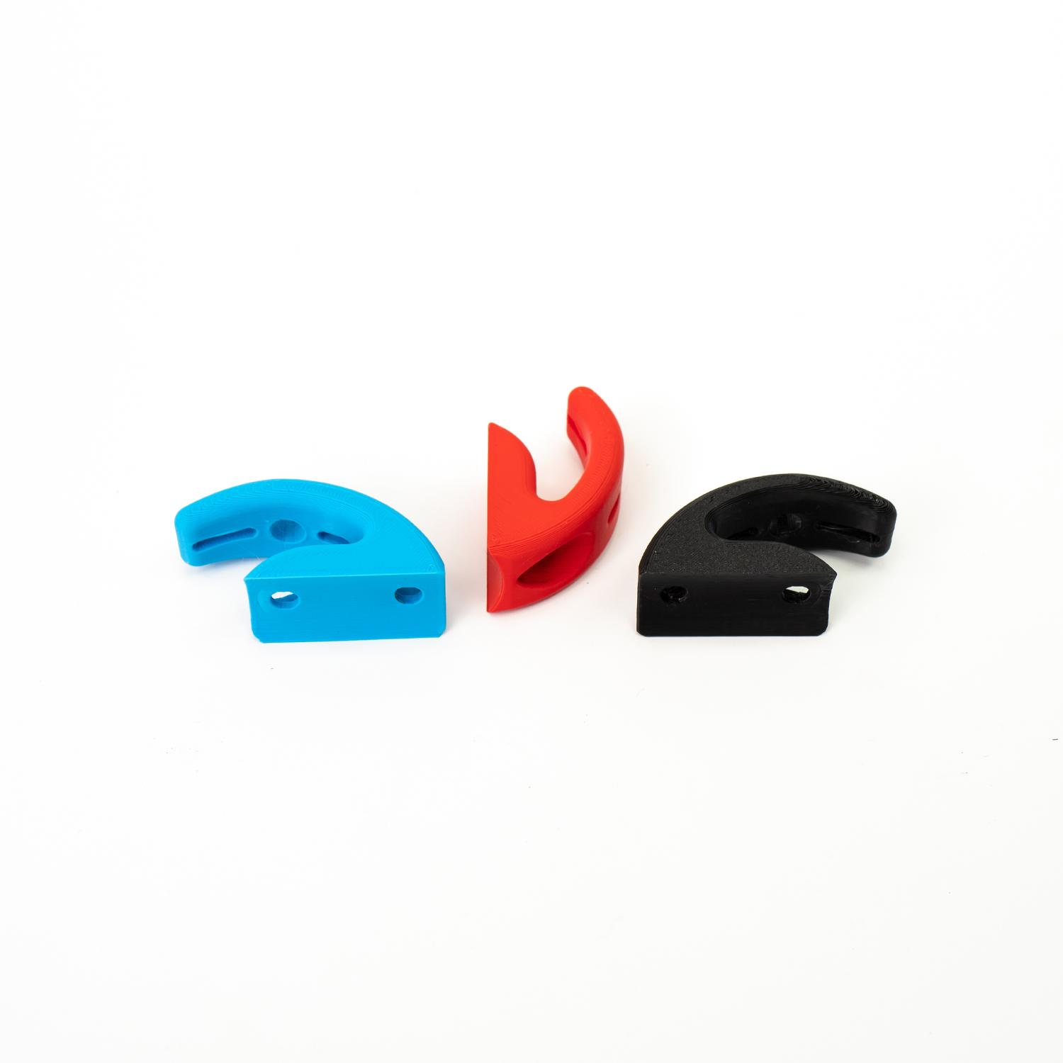 Tres ganchos de plástico de colores en azul, rojo y negro. Están sobre un fondo blanco.