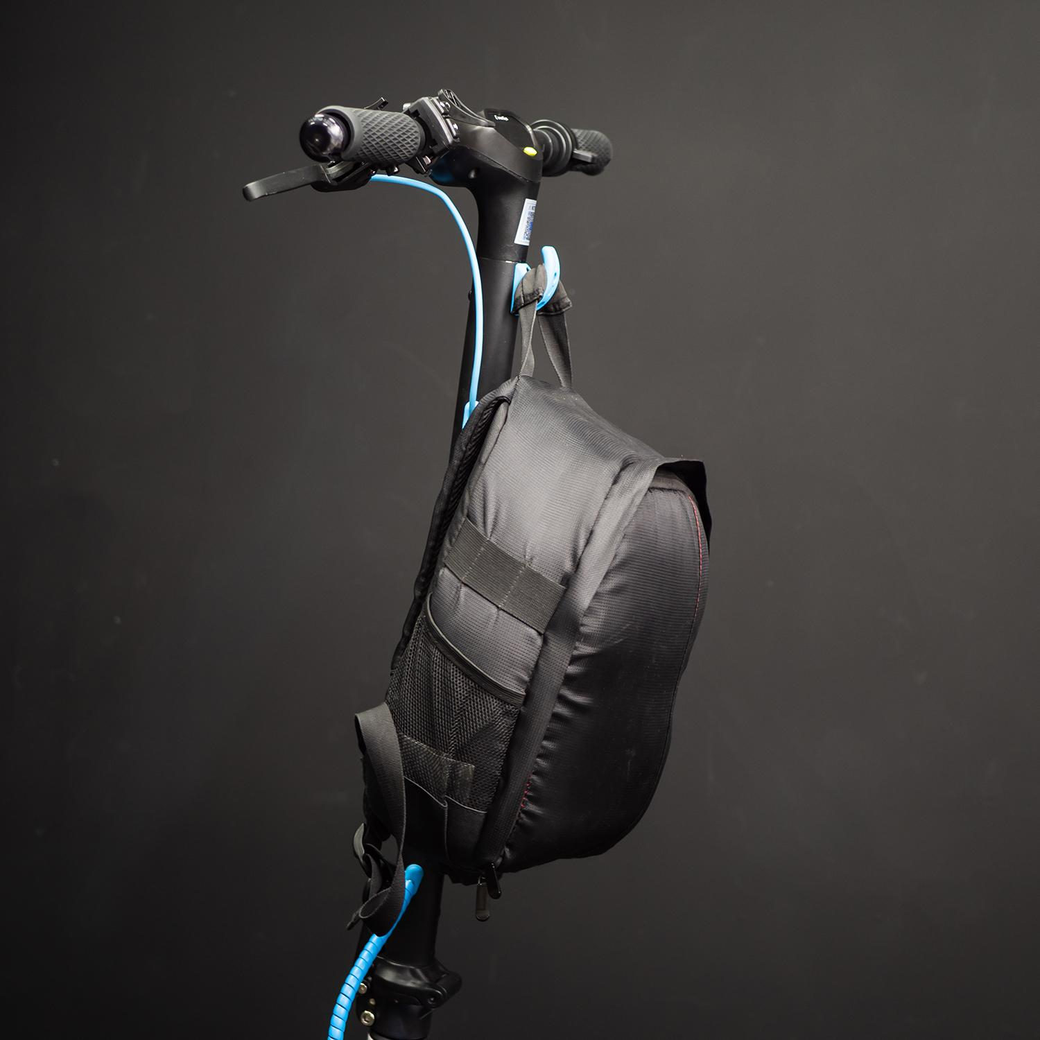 Bolsa negra sujeta al manillar de un patinete contra un fondo oscuro.