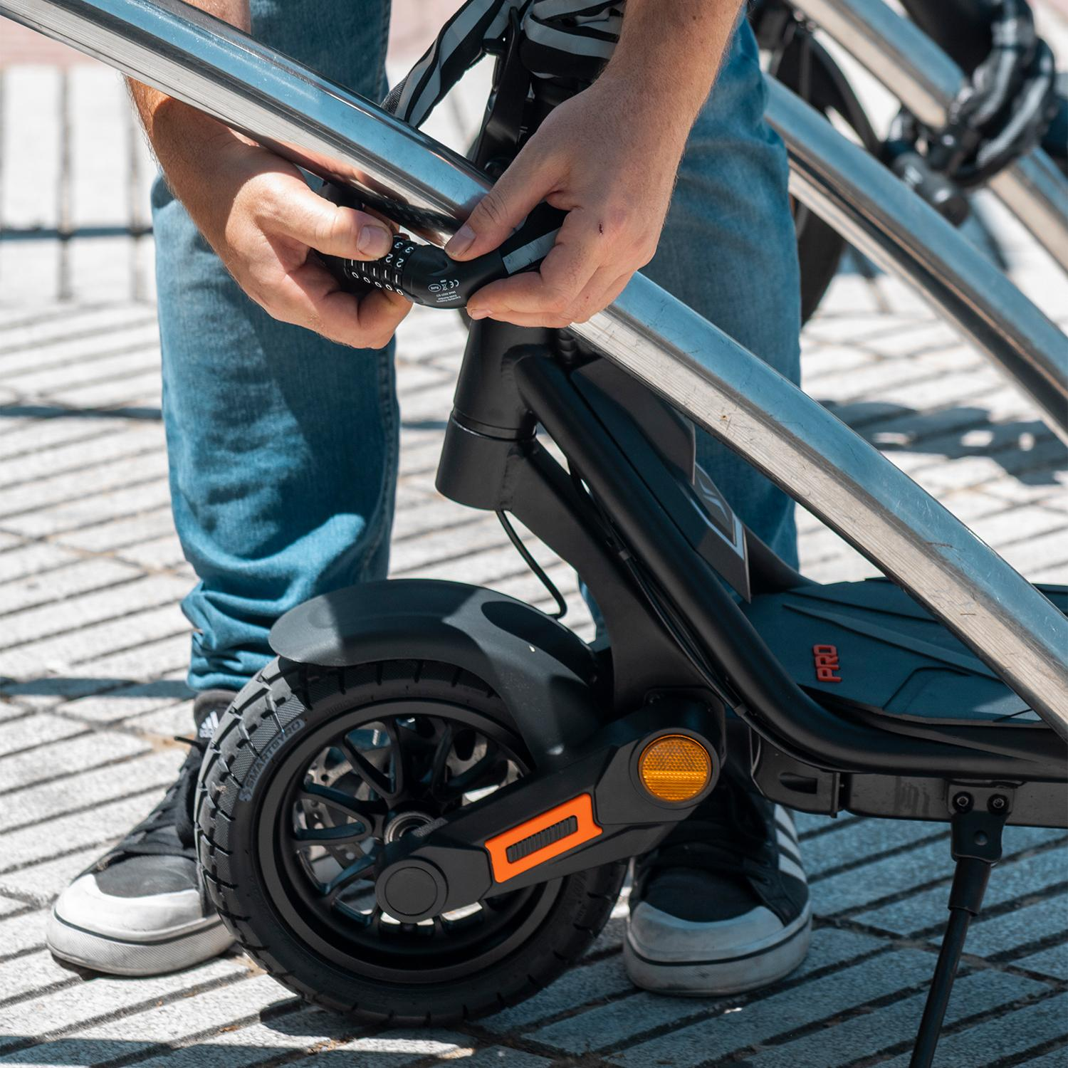 Persona desbloquea un scooter estacionado en la calle. El scooter es negro, la persona usa jeans y zapatillas.